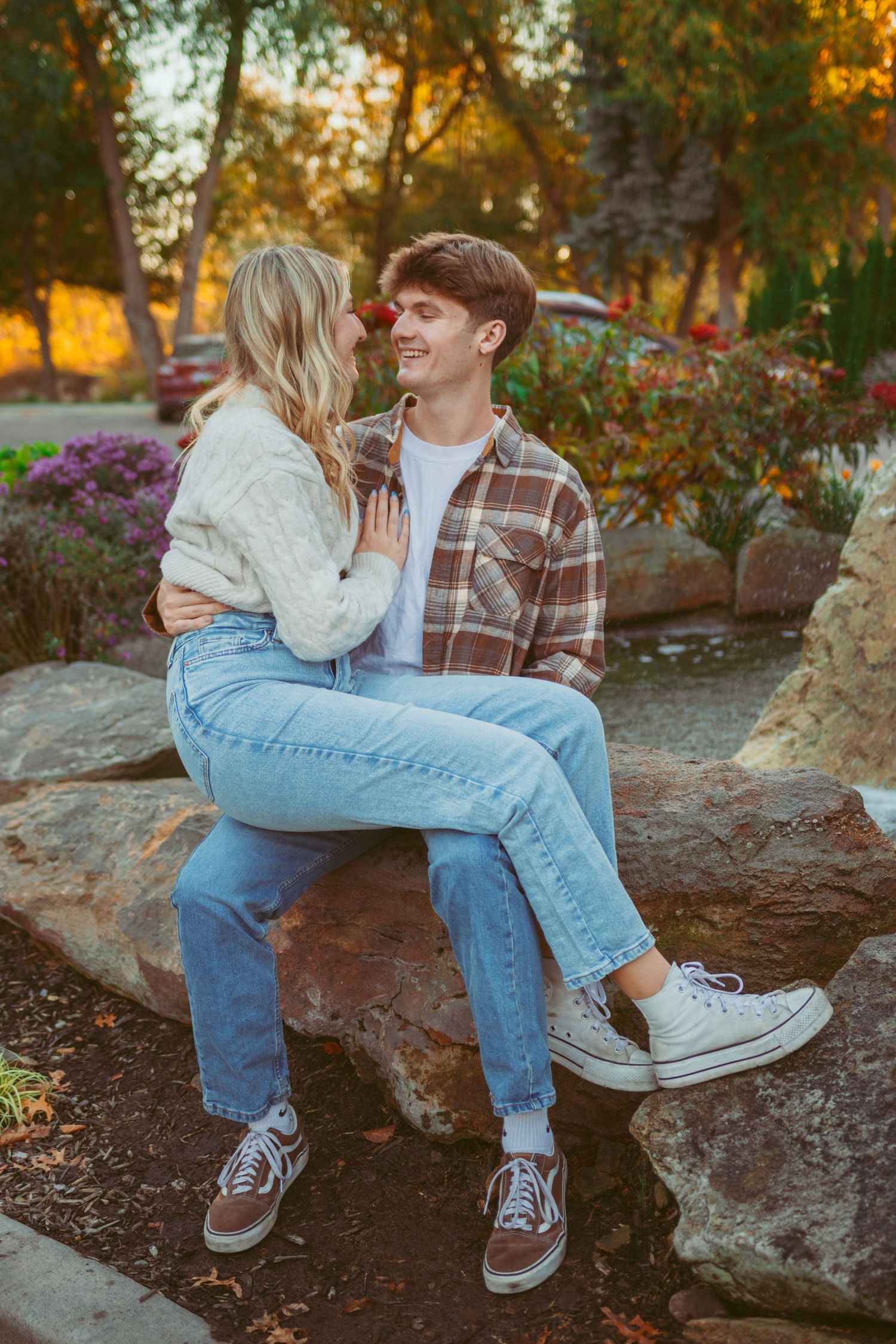 Couple sitting on large rocks in park during golden hour with autumn foliage.