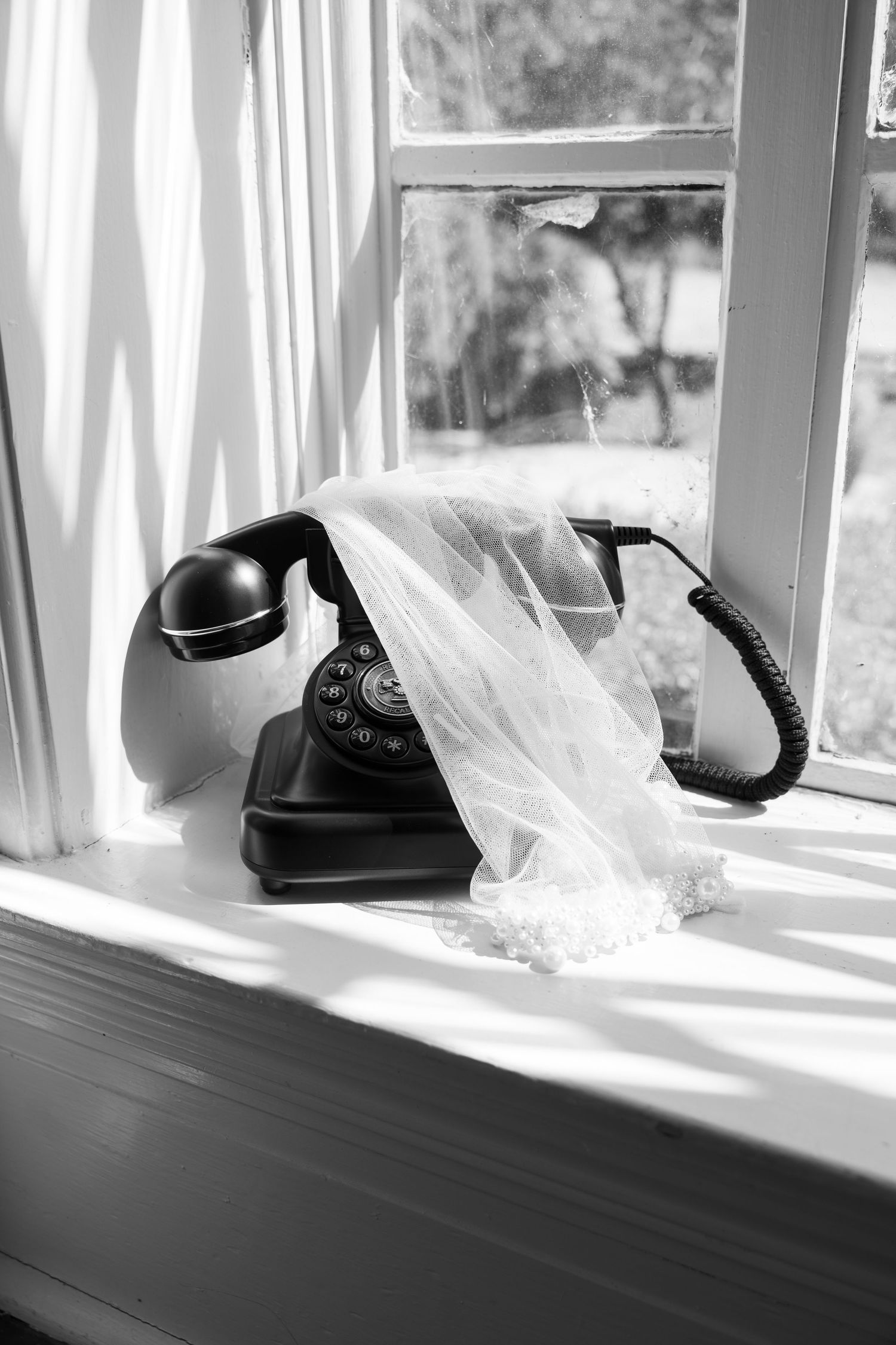 Vintage black rotary telephone on windowsill with white curtains and natural light streaming in.