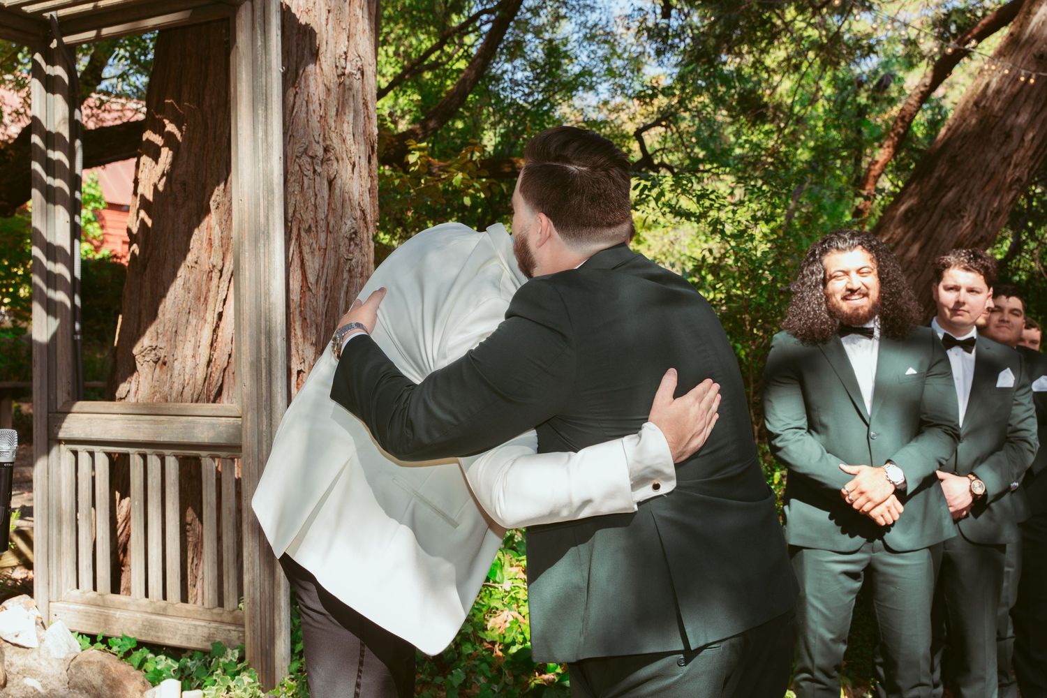 Wedding party celebrates joyfully on a rustic wooden porch surrounded by lush greenery.