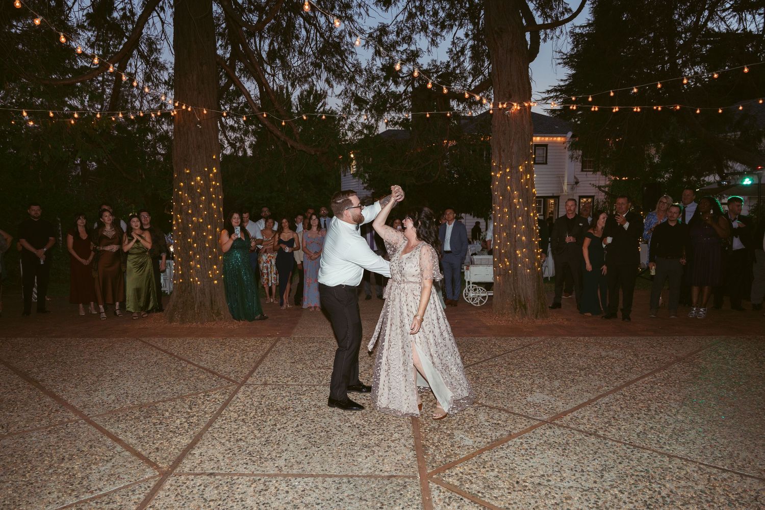 Wedding guests dancing together on an outdoor dance floor under twinkling lights.
