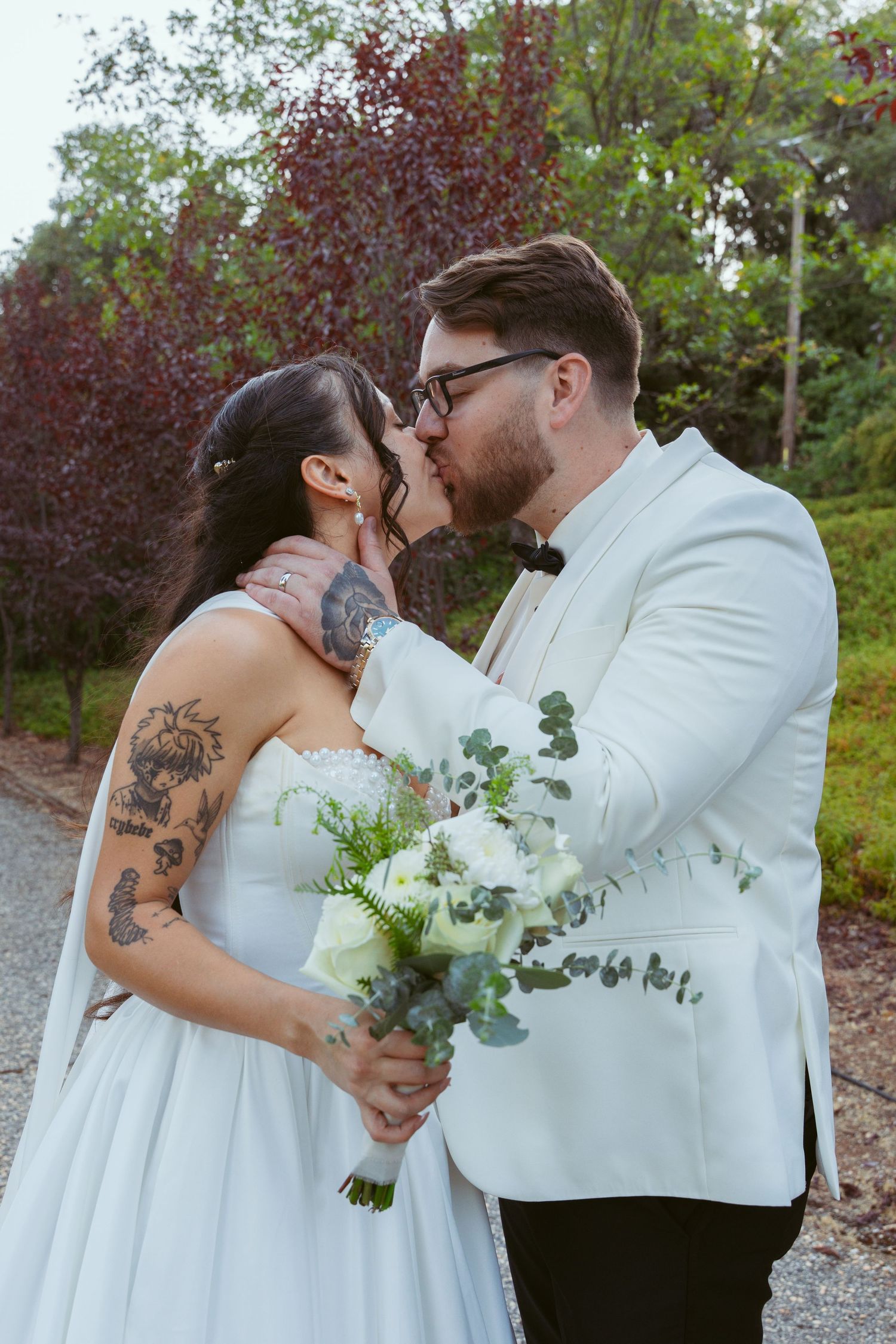 A romantic wedding couple shares an intimate moment outdoors with white floral bouquet and formal attire.