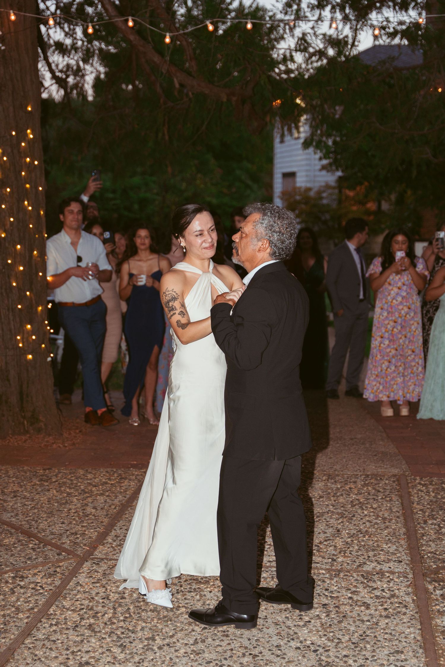 A couple shares a dance moment under string lights at an outdoor wedding reception.