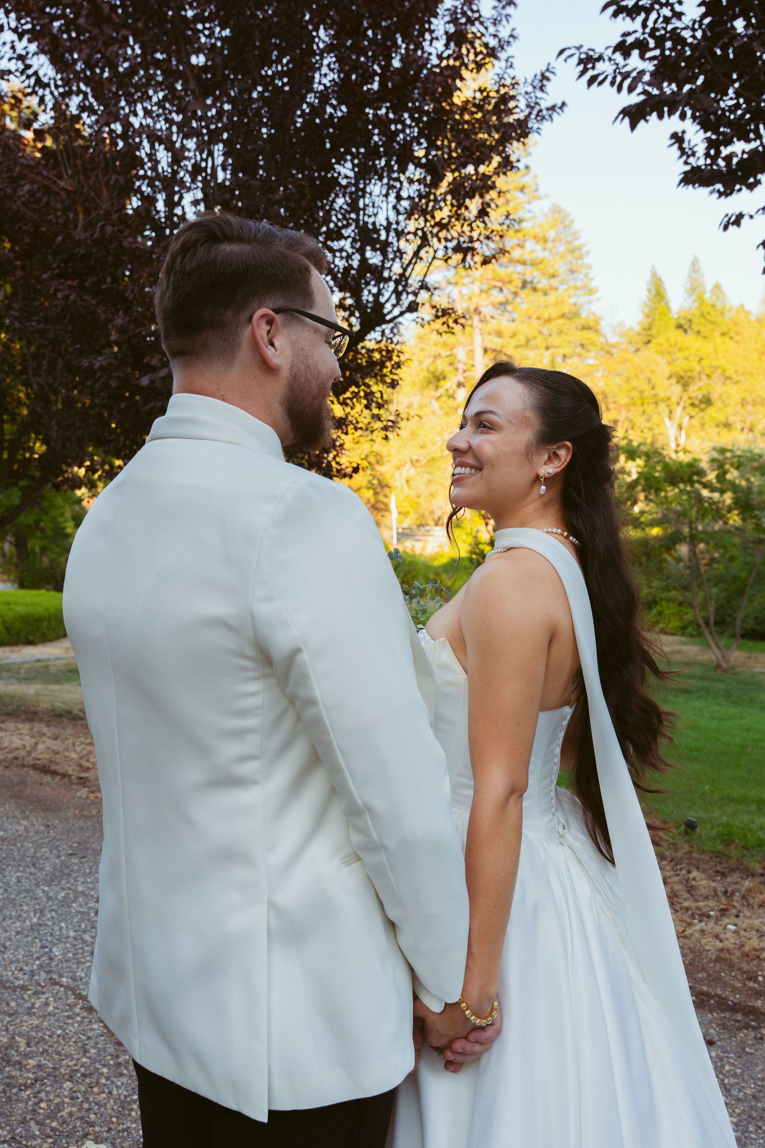 A tender moment between newlyweds holding hands on a garden path at sunset.