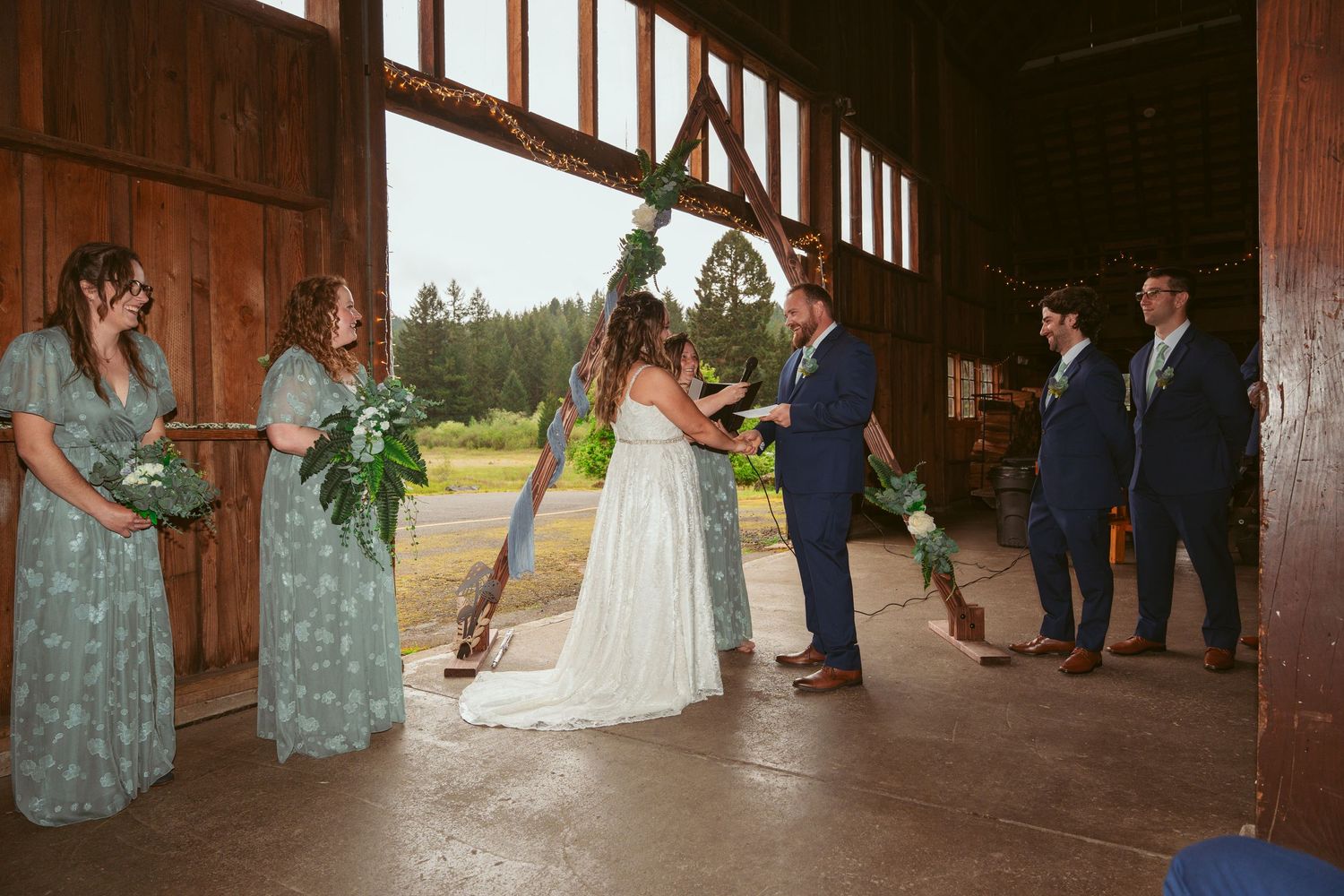 Wedding ceremony lineup inside rustic wooden barn with natural lighting.