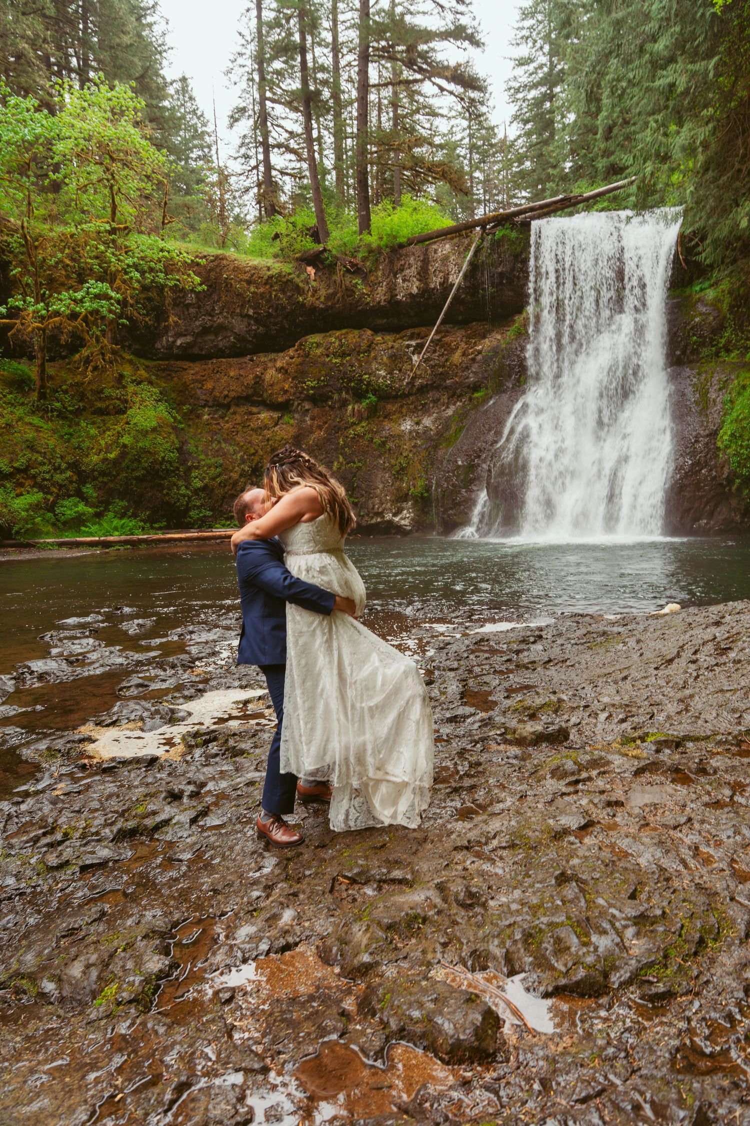 Couple dances romantically by a scenic waterfall during their wedding photoshoot.