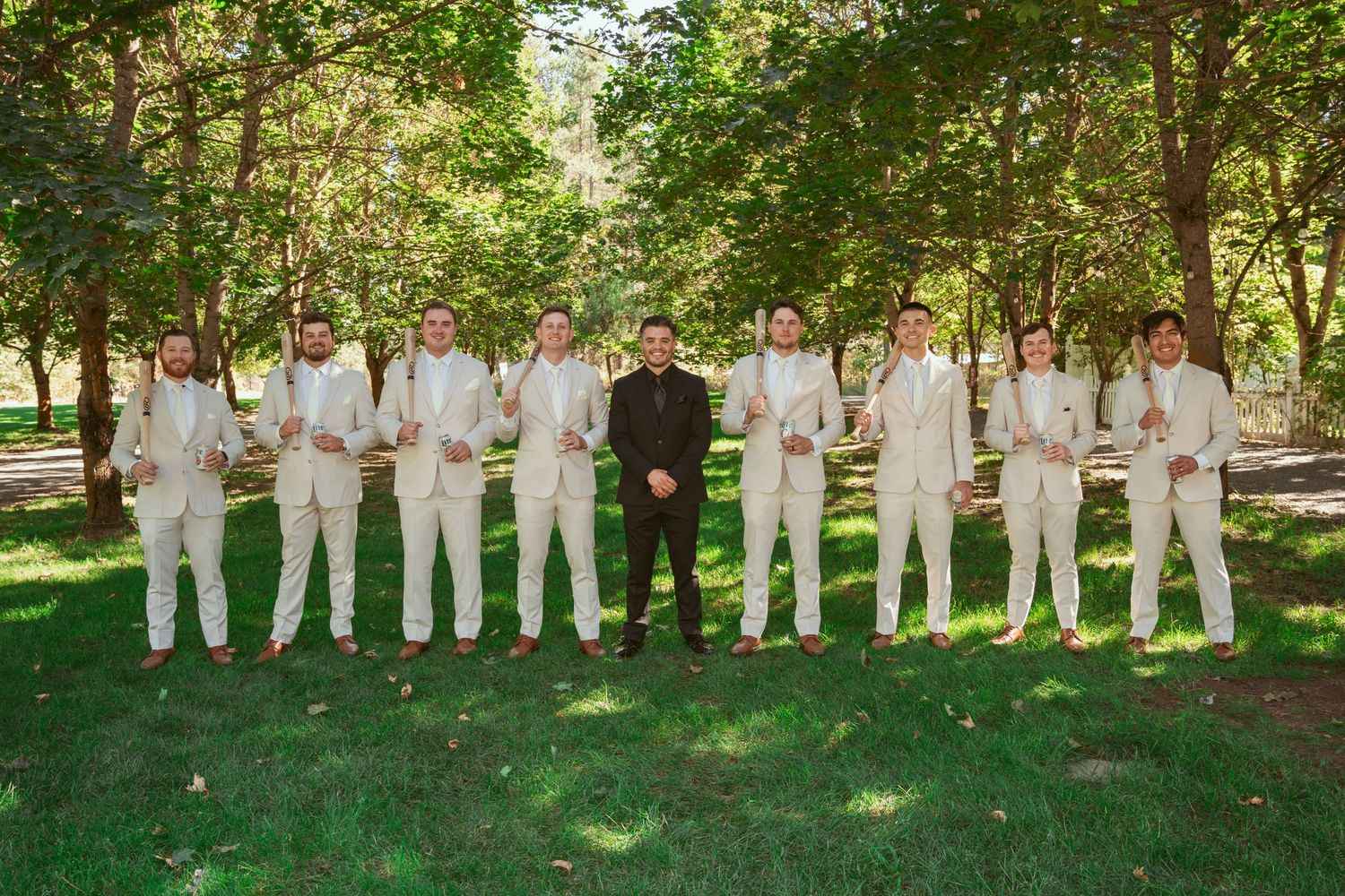 Wedding party members in cream colored suits pose in line on green lawn.