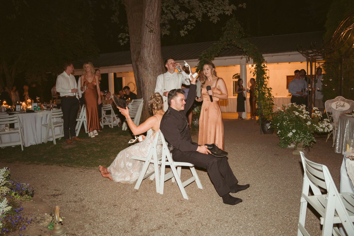 Outdoor wedding reception setup with white chairs and ambient lighting at dusk.