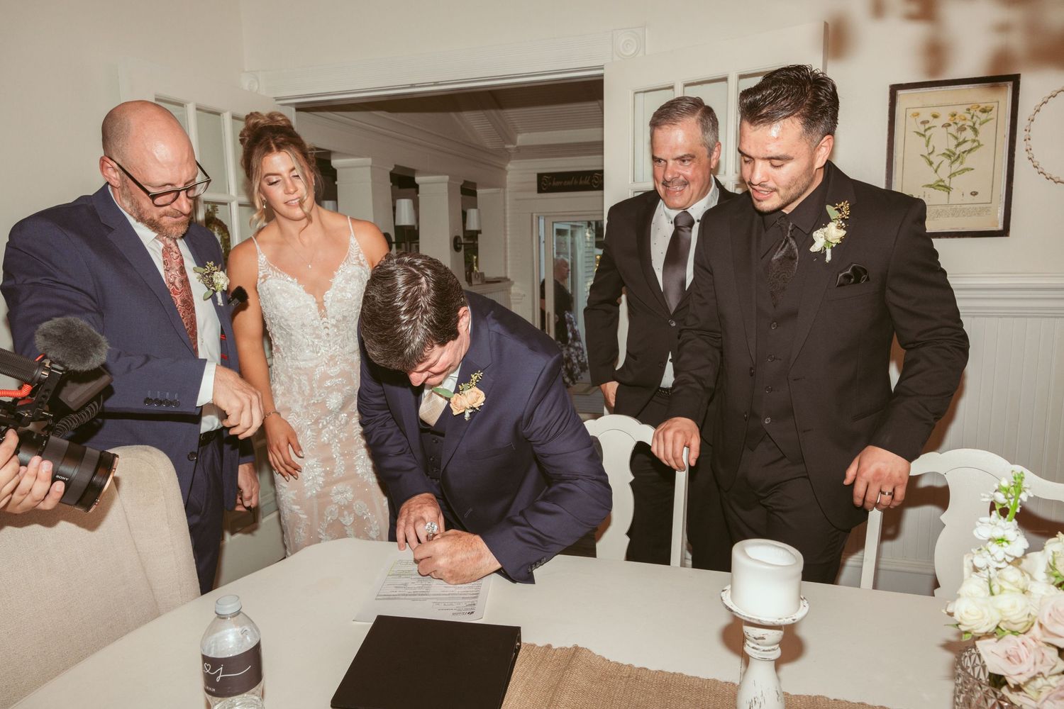 Wedding party members signing documents at an indoor reception venue.