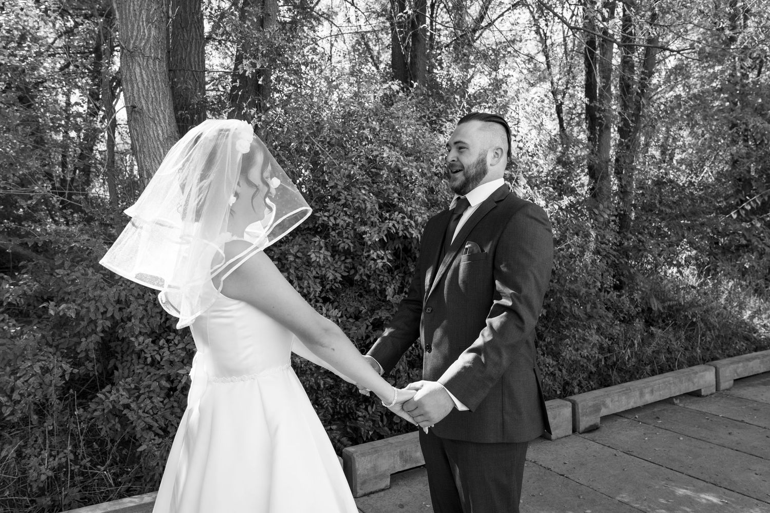 A black and white photo of a couple holding hands during their first look wedding moment.
