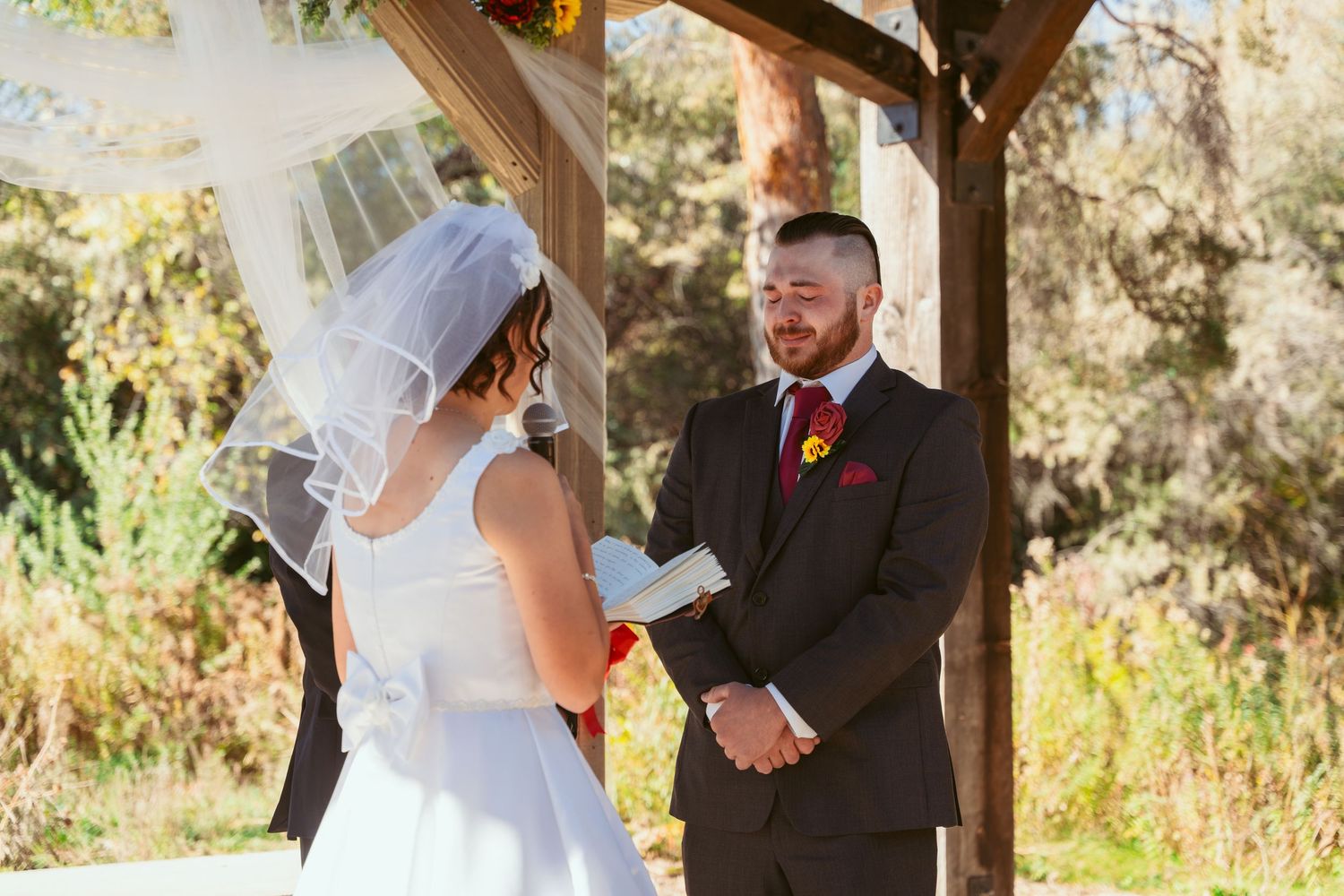 Emotional outdoor wedding ceremony moment under a wooden pergola with autumn scenery.