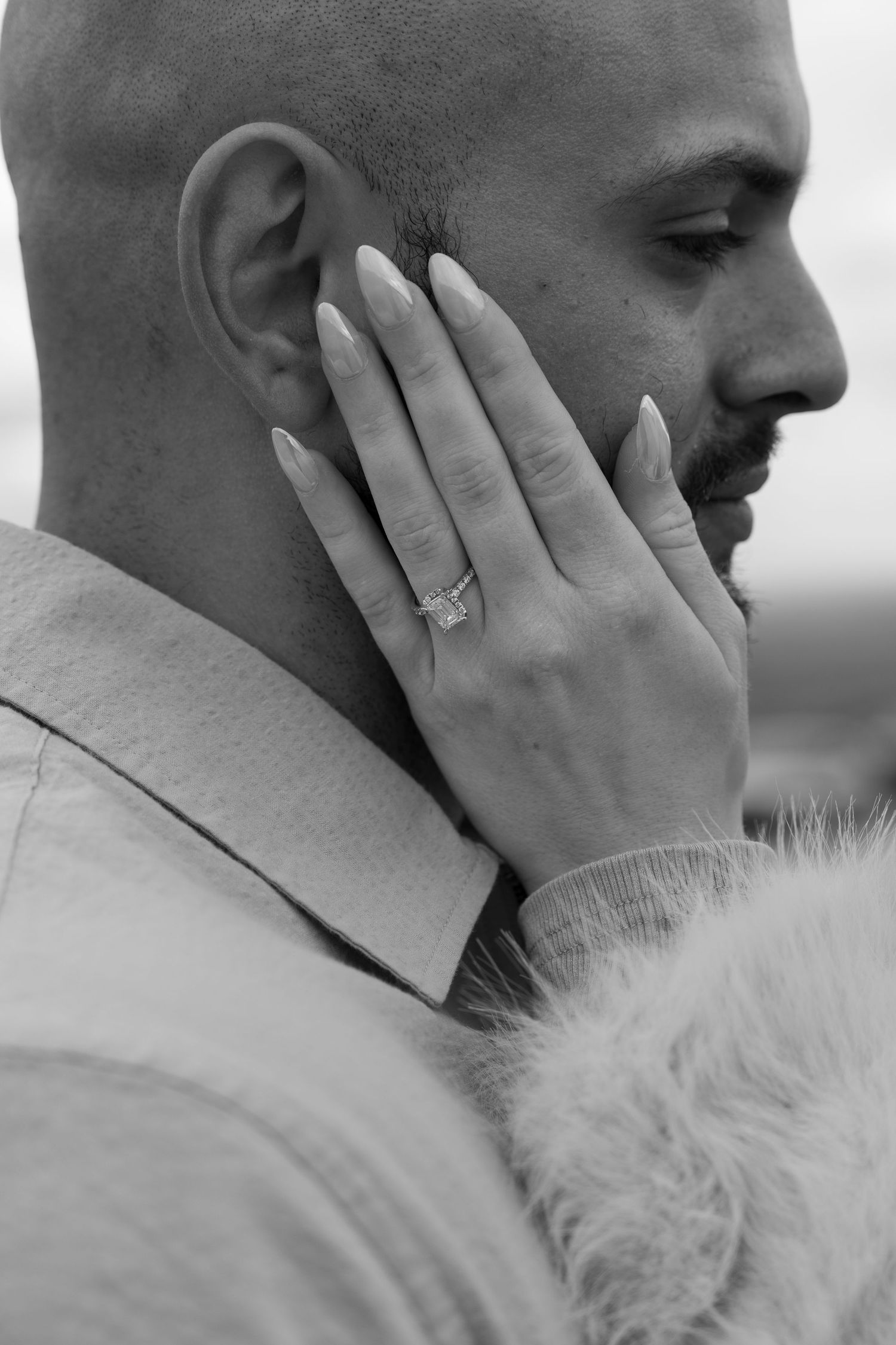 Close up black and white photo showing a hand with an engagement ring against a person's face.
