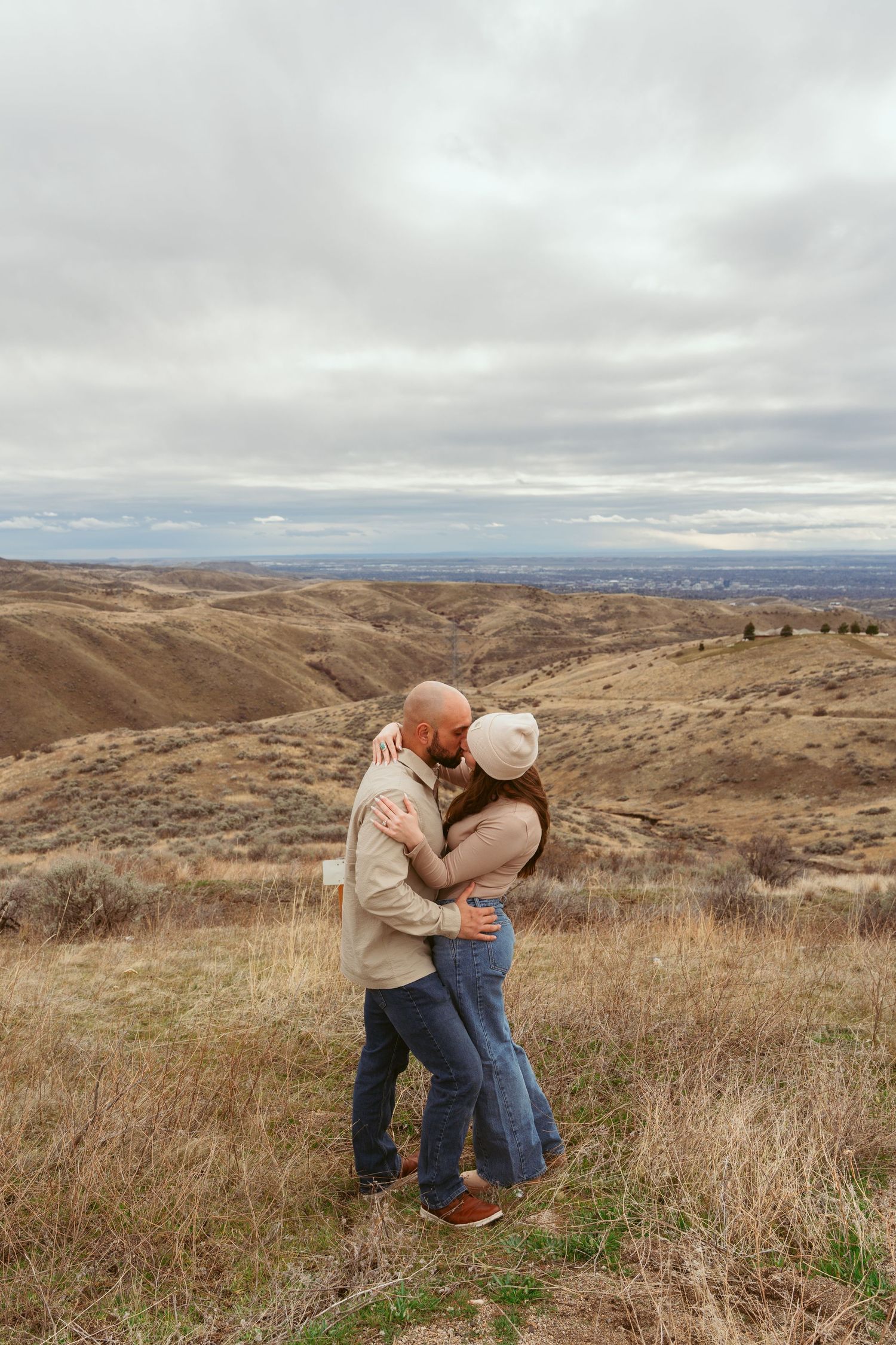 Couple sharing tender moment while dancing on hillside with dramatic cloudy sky.