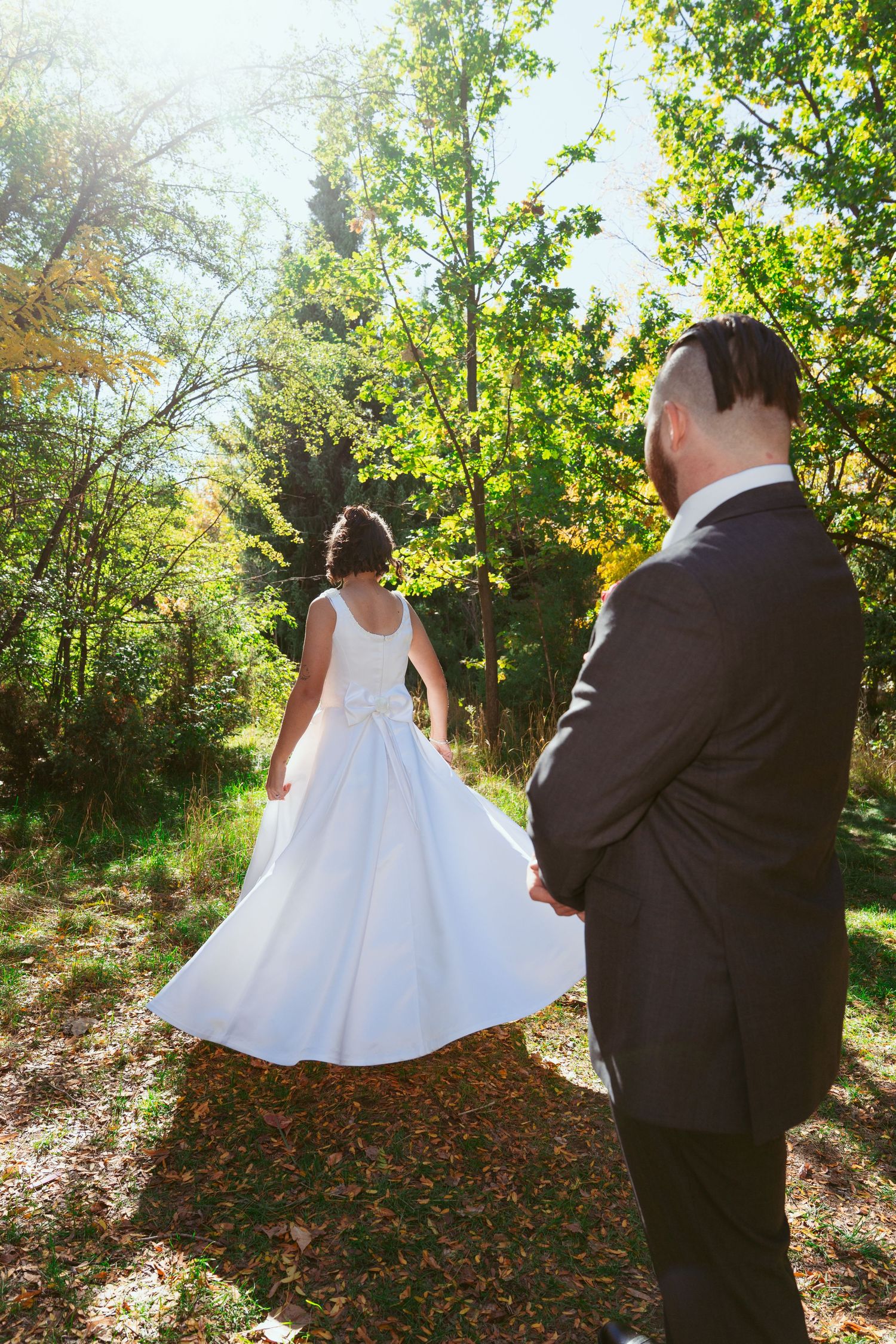 Wedding couple poses in sunlit garden with flowing white dress.