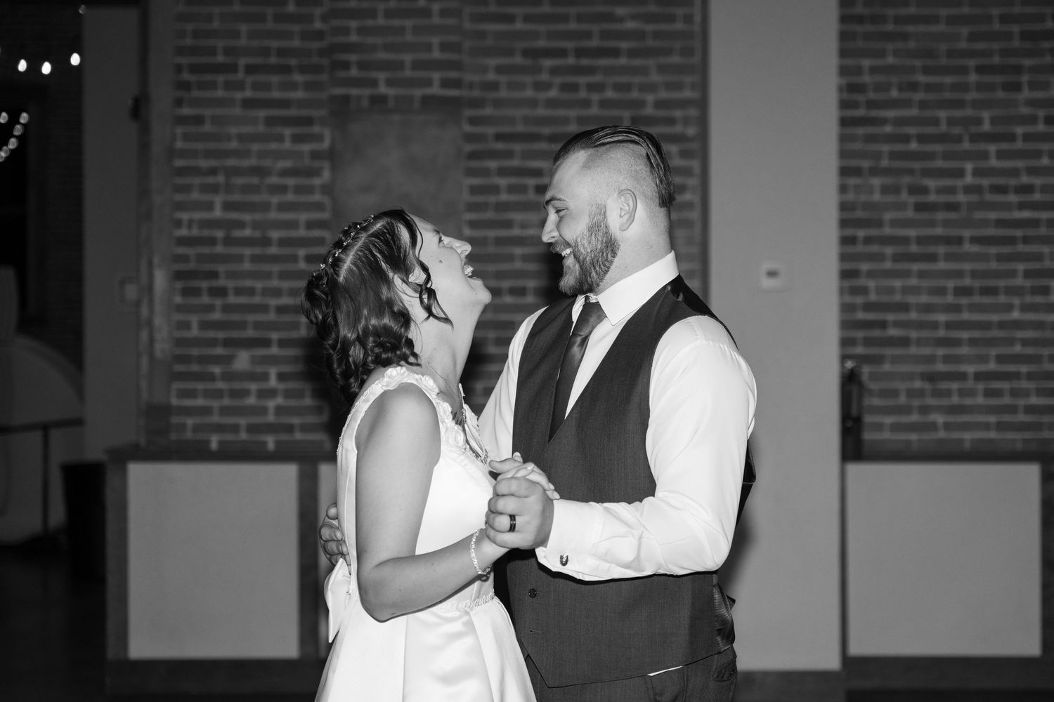 A couple shares an intimate dance moment in black and white against exposed brick walls.