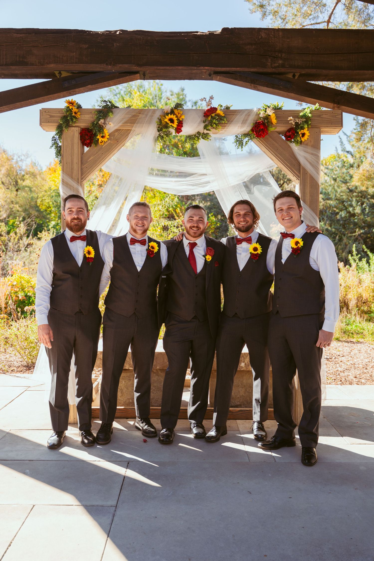Groomsmen in matching vests and ties pose under covered outdoor wedding venue.