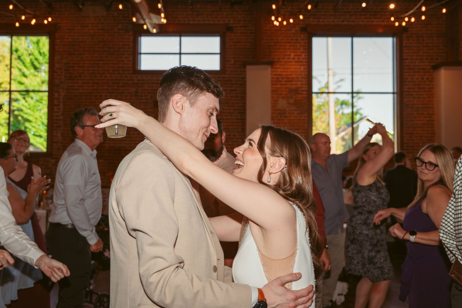 Wedding guests dancing together in a rustic brick venue with string lights overhead.