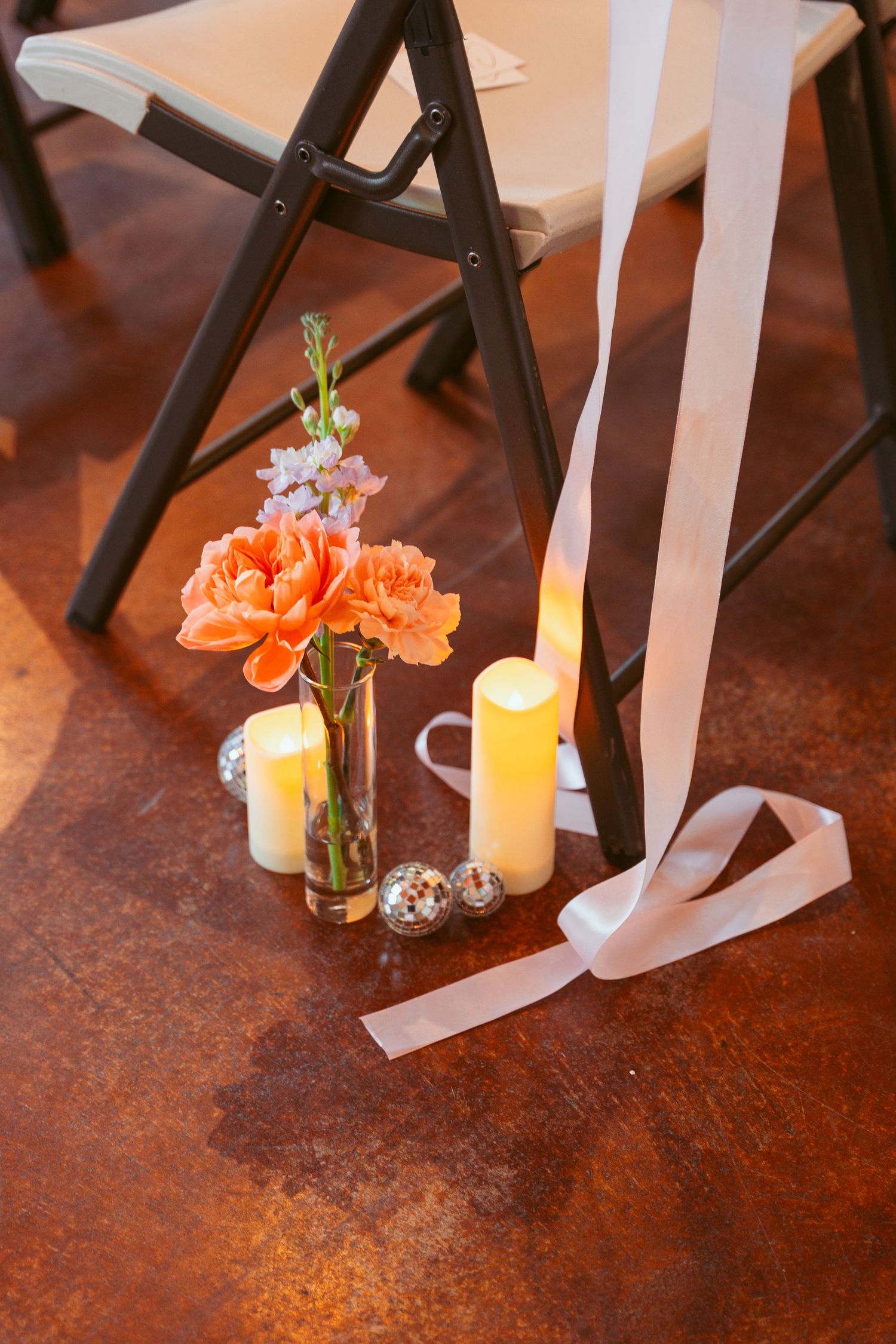 Orange floral arrangements with candles and white ribbons decorating ceremony aisle chairs.