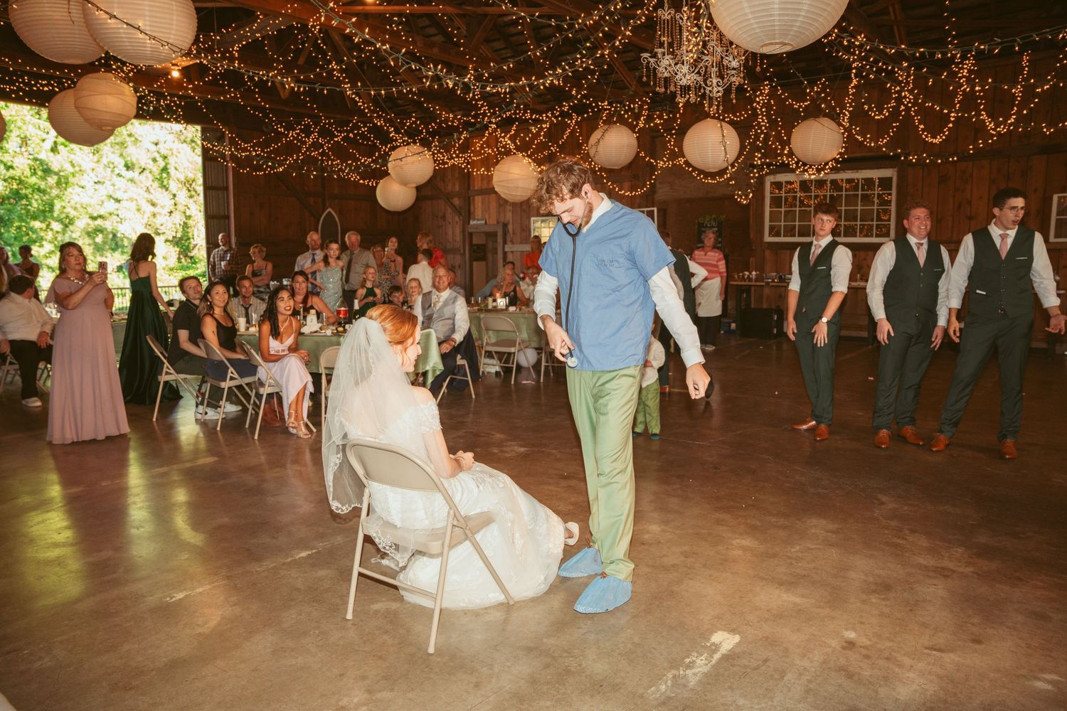 Wedding celebration with guests dancing under romantic lighting in a decorated barn venue.
