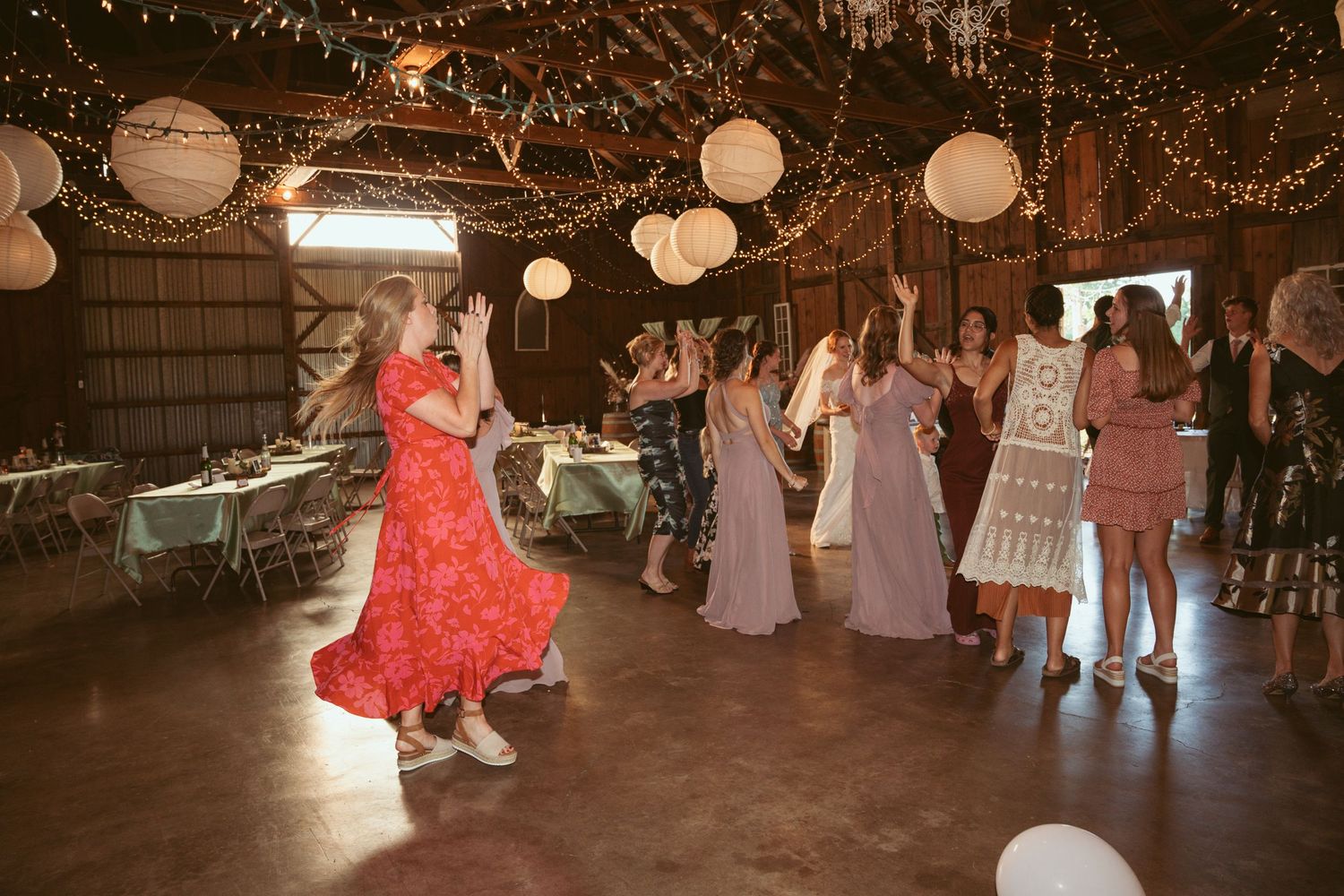 Lively wedding reception dance floor with guests dancing under decorative lighting and lanterns.