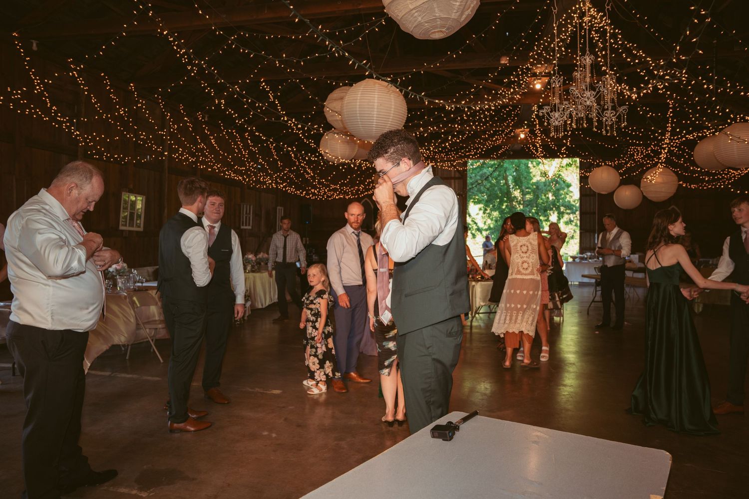 Guests dance beneath a canopy of string lights and white paper lanterns at an indoor venue.