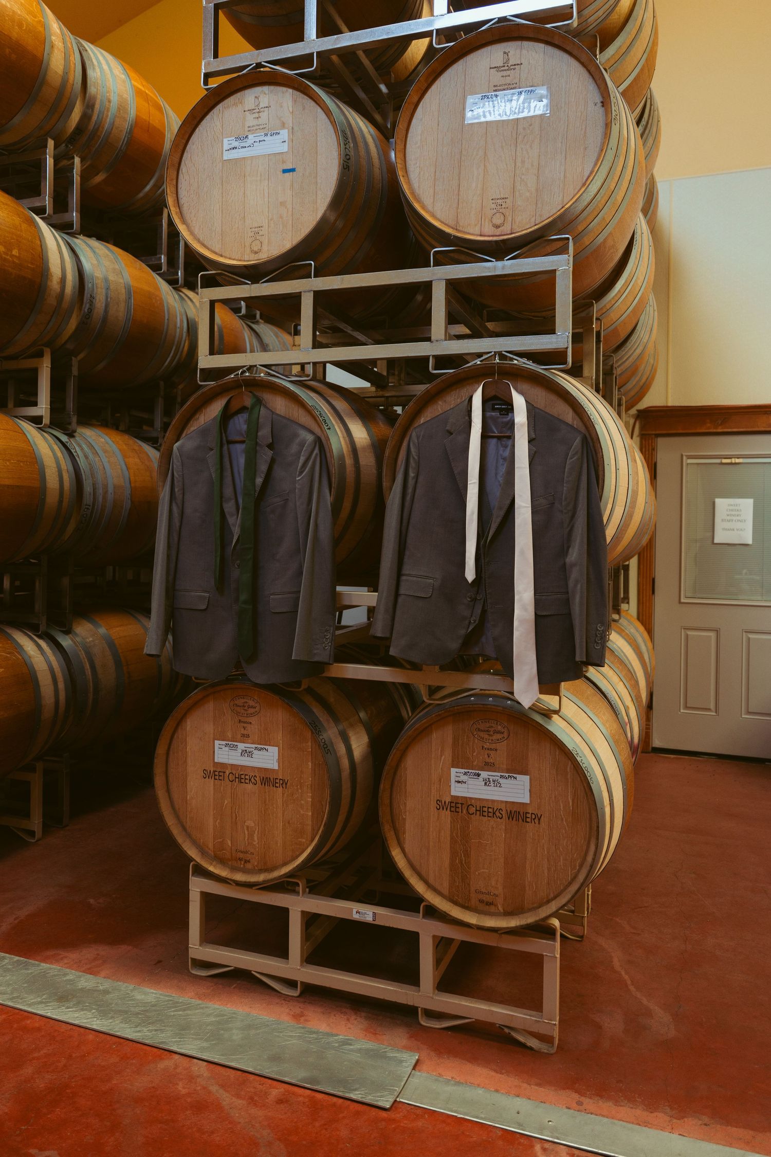 Wine barrels stacked with formal suits displayed in a cellar setting.