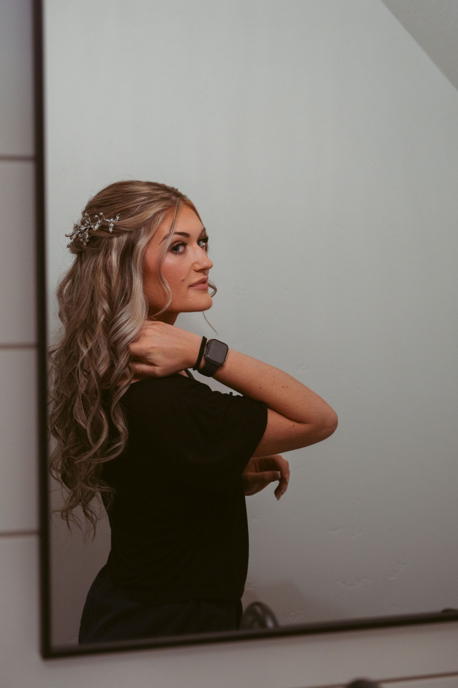 A woman in a black shirt with wavy blonde hair poses against a white wall in an artistic photo sequence.