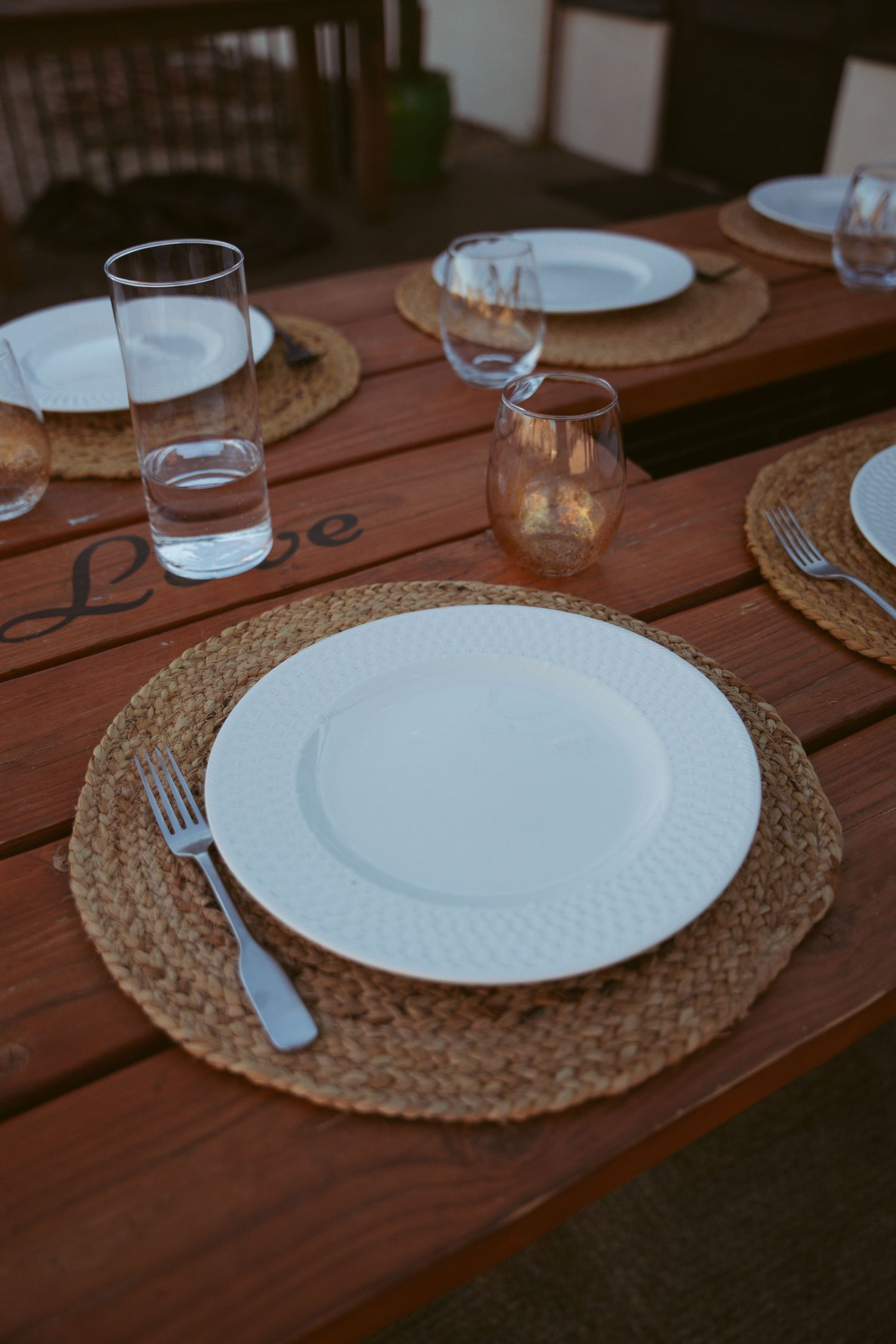 Table setting with white plates on woven placemats and wooden surface.