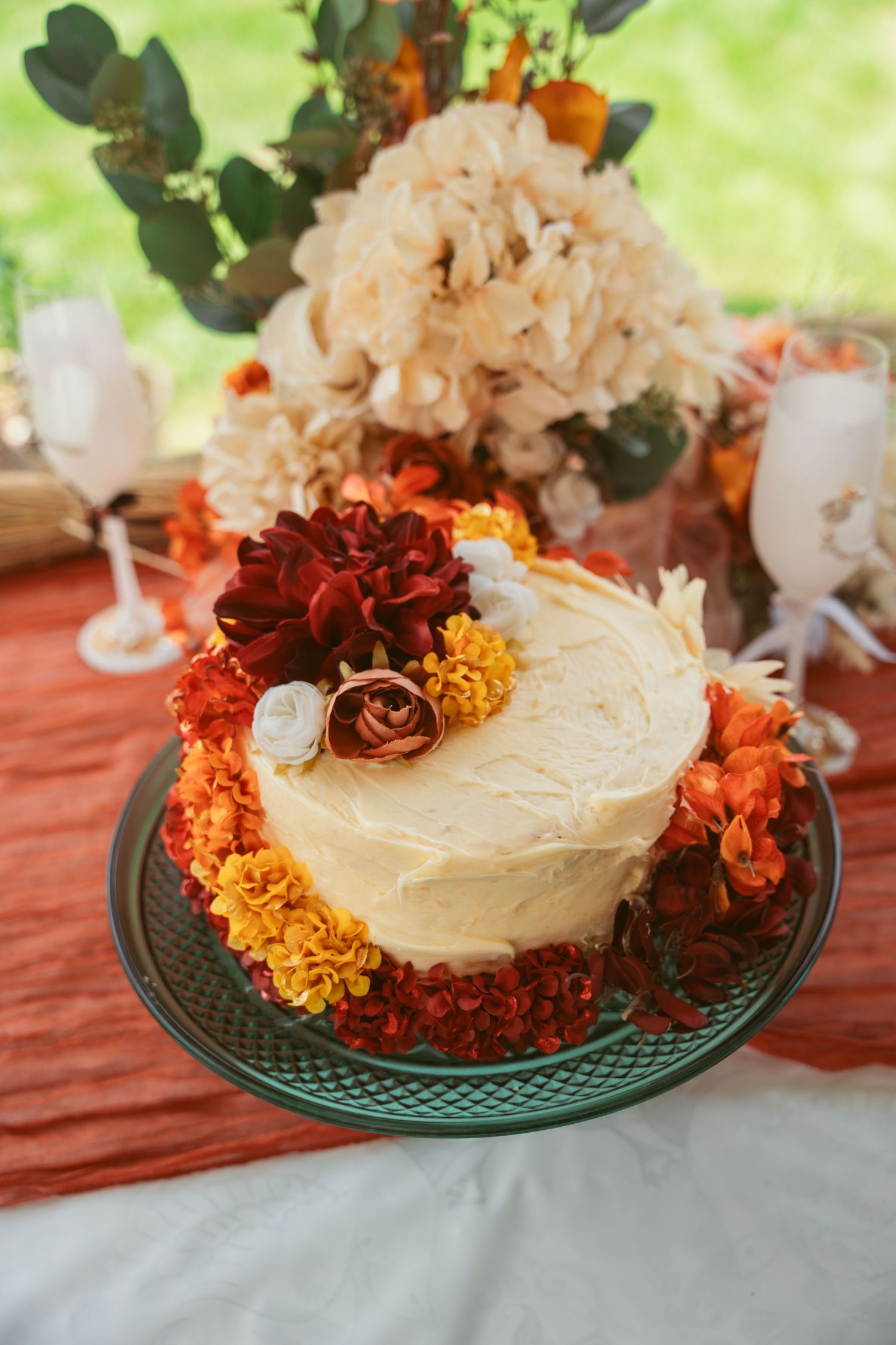A white frosted cake decorated with orange and burgundy flowers sits on a green plate.