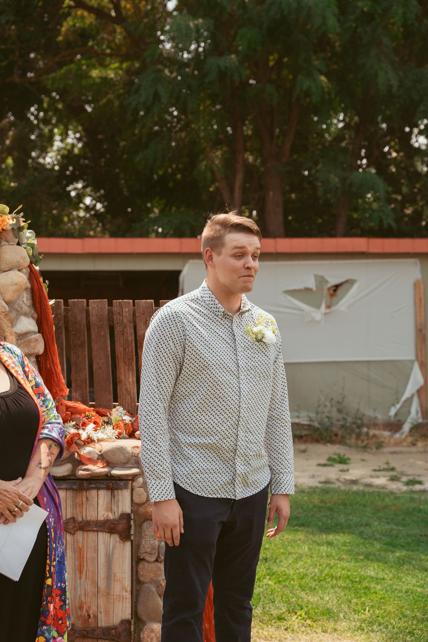 Wedding party members reading from papers during an outdoor ceremony with a wooden fence backdrop.