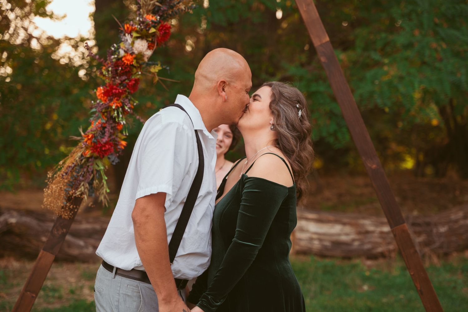 Newlyweds share an intimate kiss beneath a rustic wooden ceremony arch.