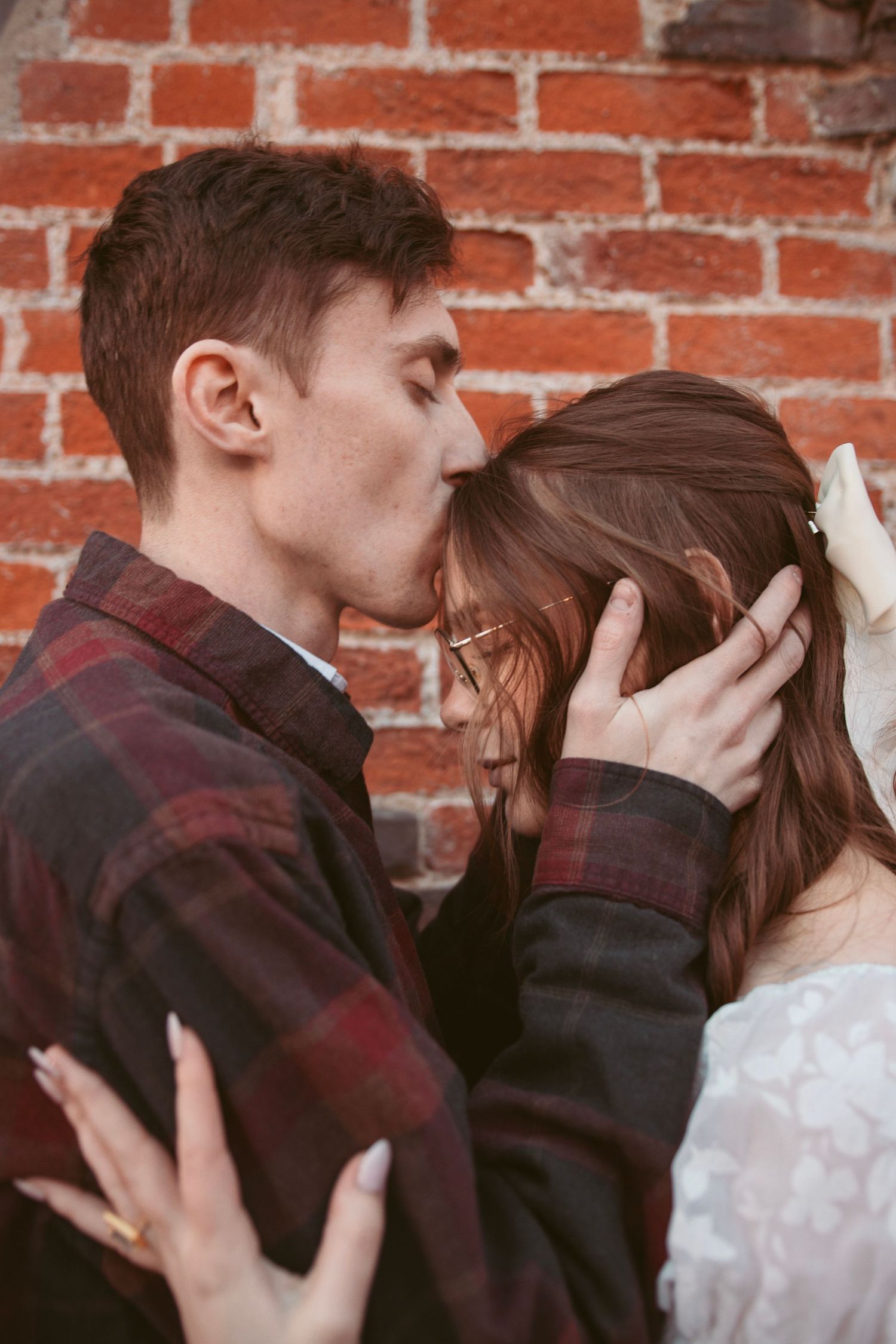 Tender moment shared between two people in front of rustic brick wall.
