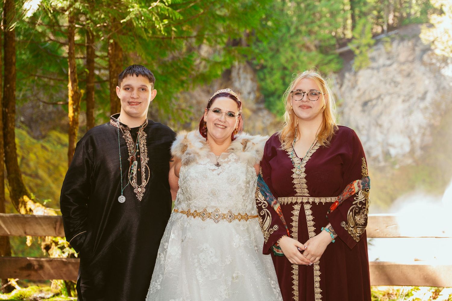Wedding party members pose in coordinated medieval-style burgundy and cream outfits in a forest.