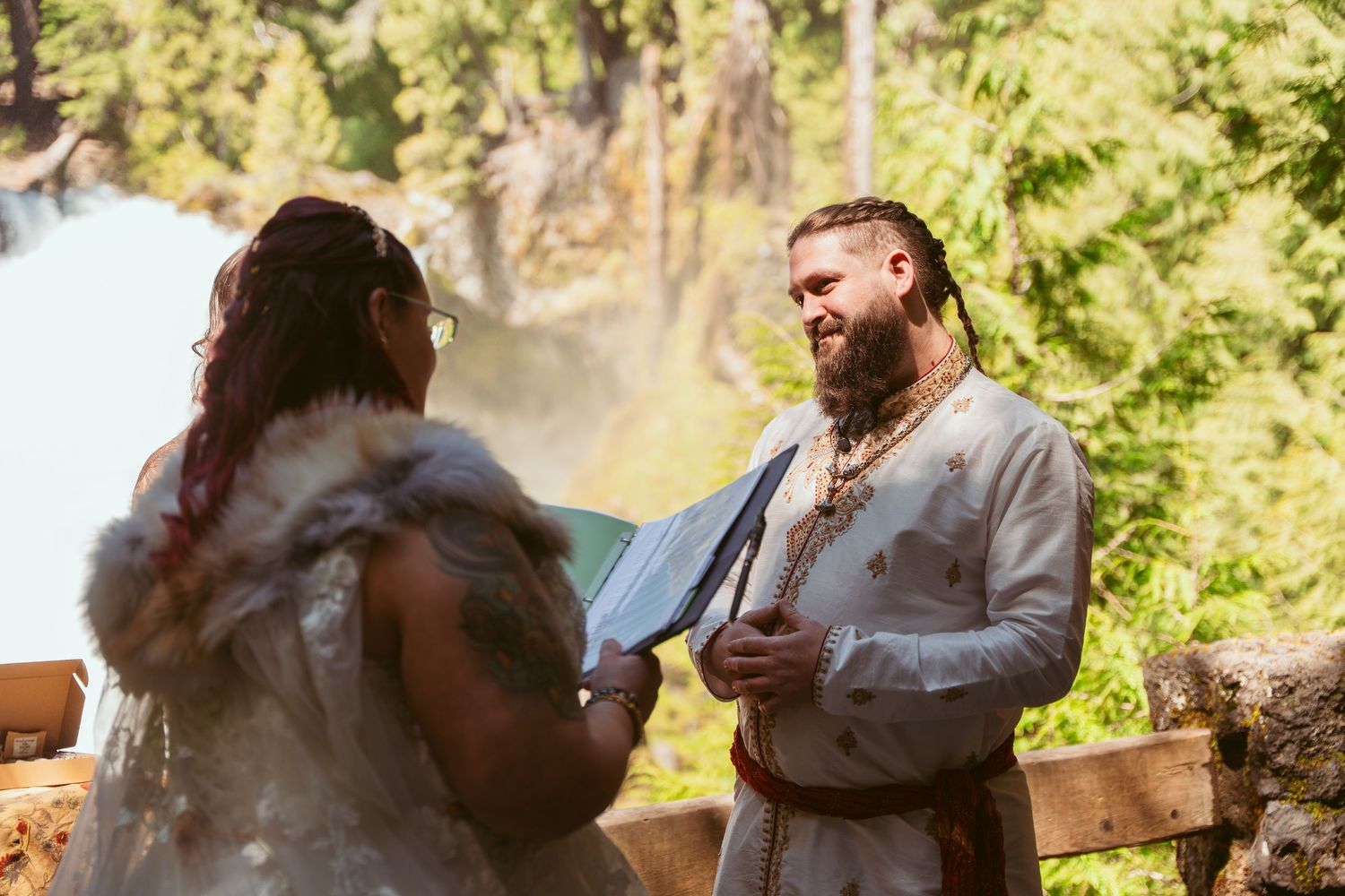 A couple shares their first dance at a woodland wedding ceremony with sunlit trees in the background.