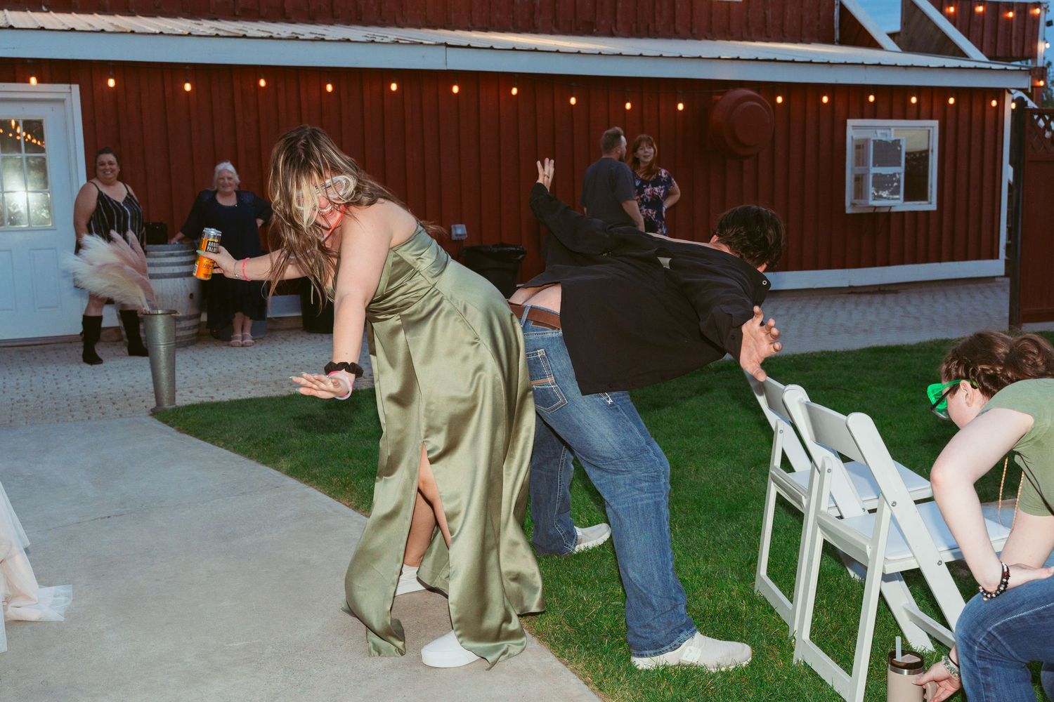People dancing and celebrating at an outdoor wedding venue with string lights and a red barn.