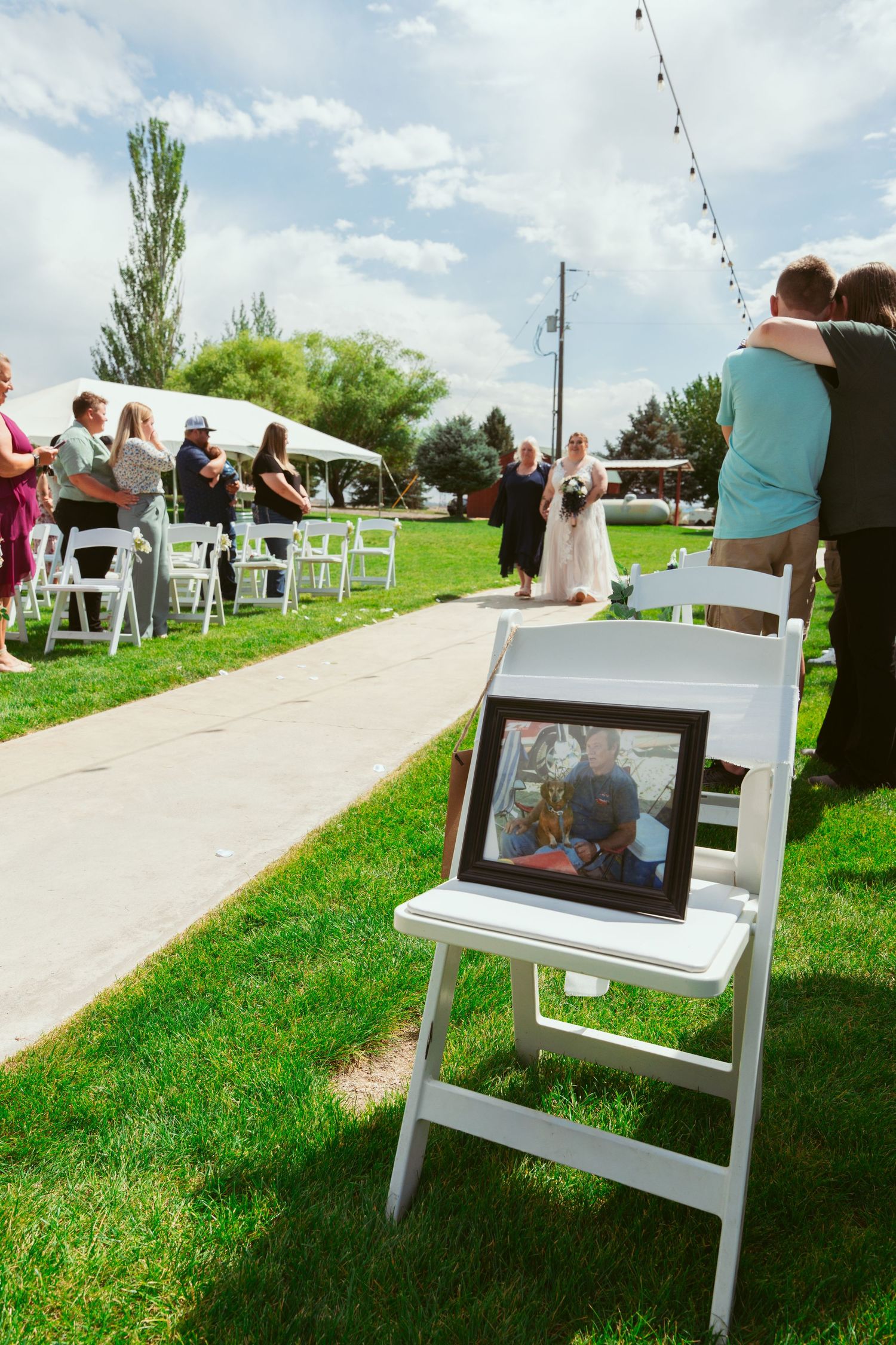 Empty white folding chairs set up on grass lawn for outdoor ceremony with cloudy sky.
