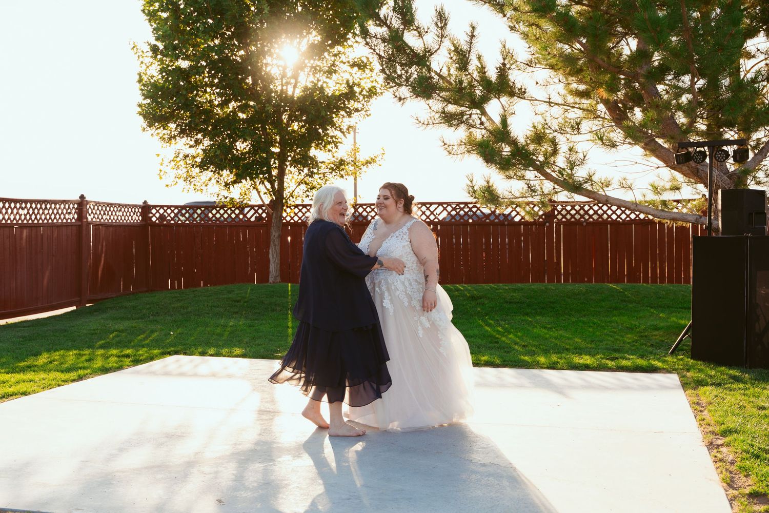Wedding guests dance in a line formation on a patio during an outdoor reception at sunset.