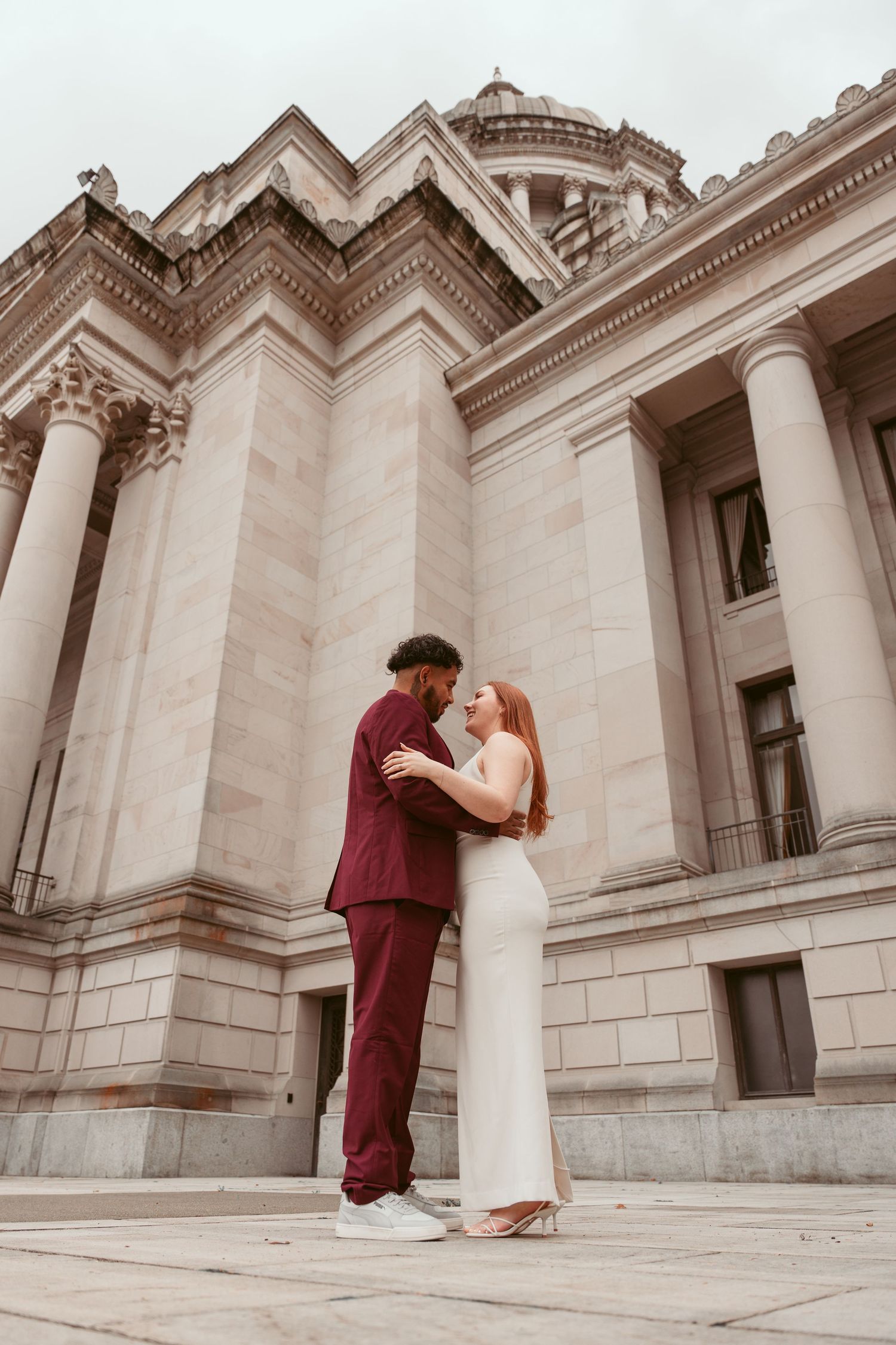 A romantic couple poses outside a neoclassical building with grand columns and architectural details.