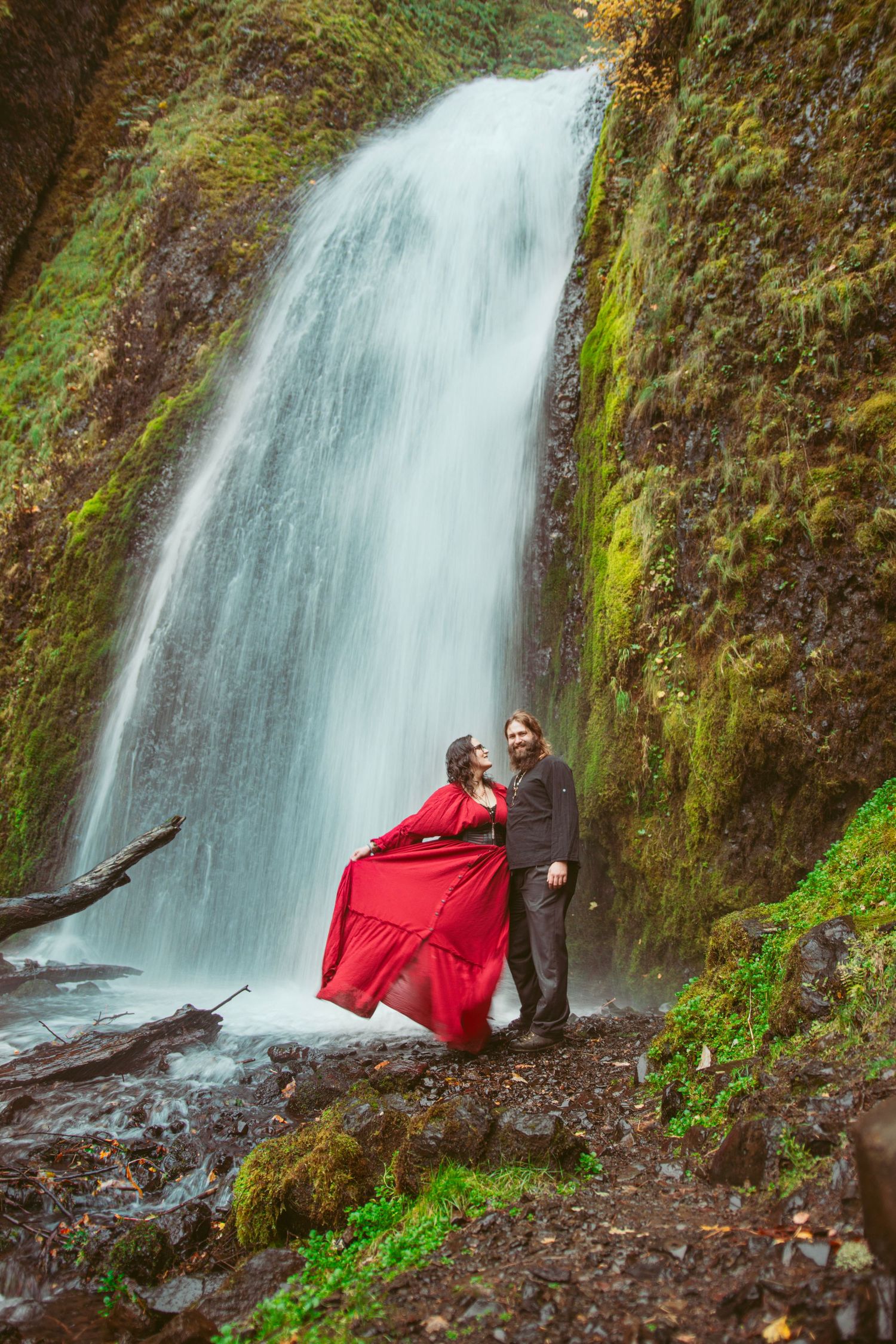 Flowing waterfall creates stunning backdrop for romantic photoshoot in natural setting.