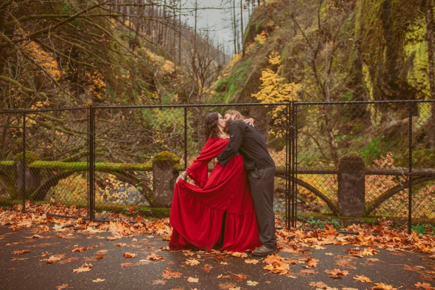 Autumn engagement photos with dramatic poses along a scenic waterfall trail.