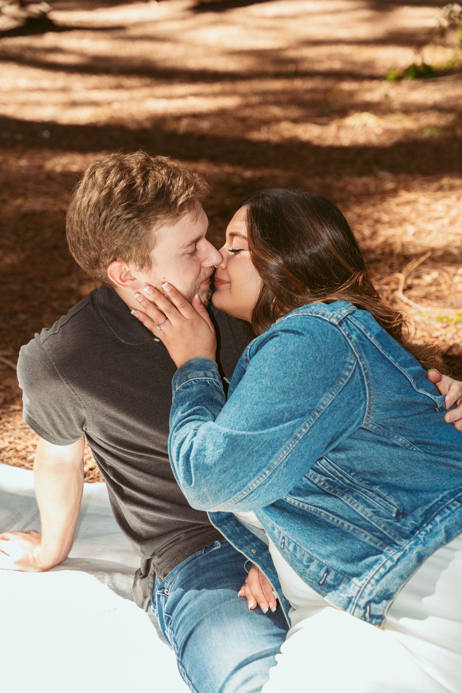 Romantic moment captured between two people on a white blanket in a forest setting.