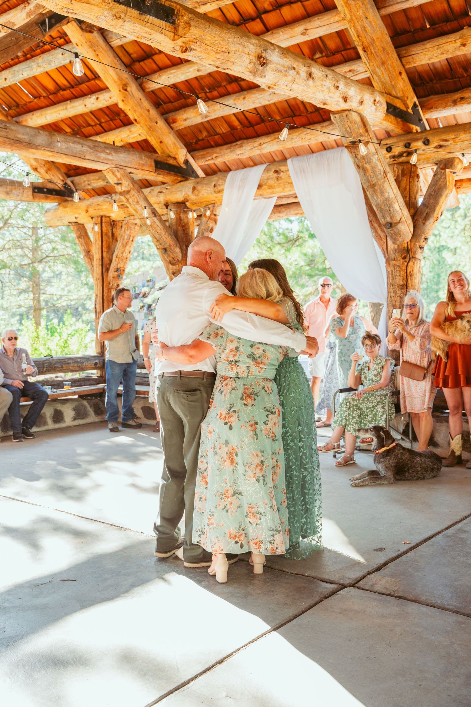Guests watching a couple dance in a rustic pavilion with exposed wooden beams.
