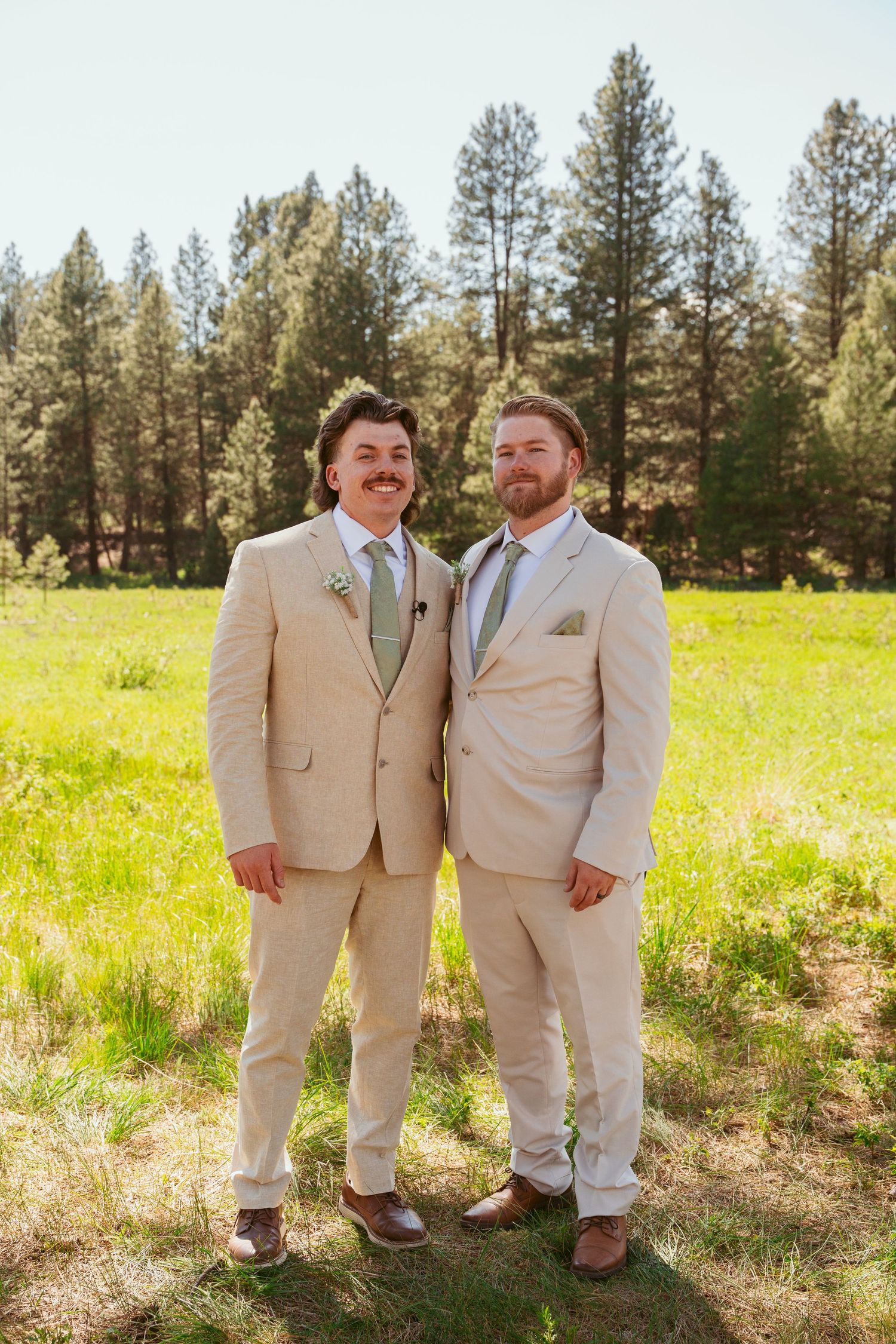 Groomsmen in beige suits share candid moments in a sunlit forest setting.