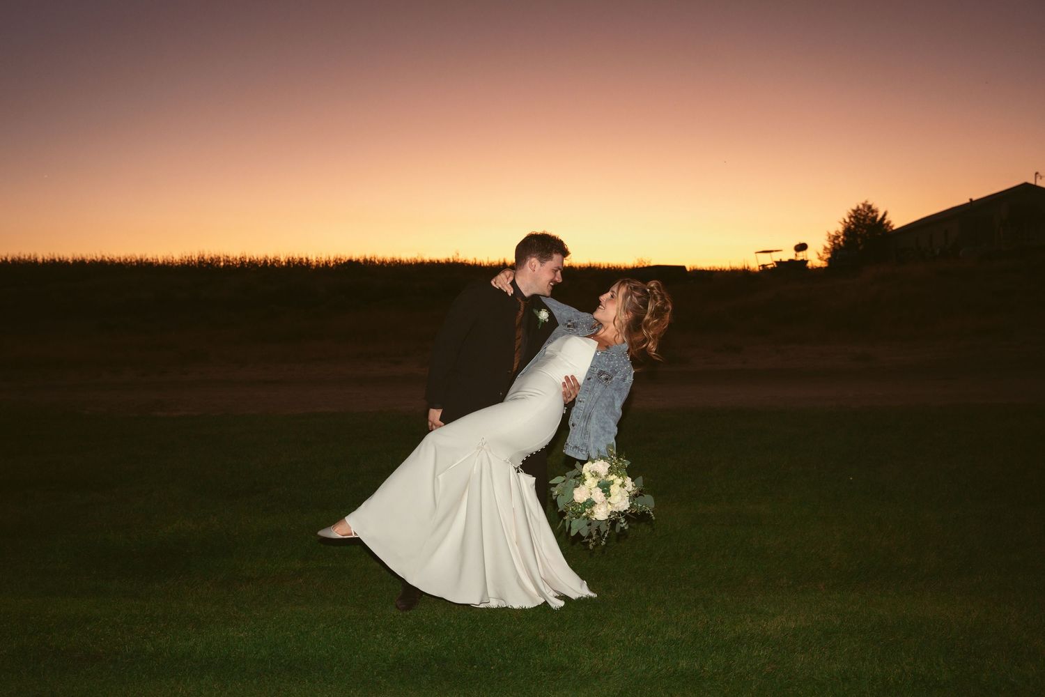 A couple dances together in a field during a golden sunset on their wedding day.