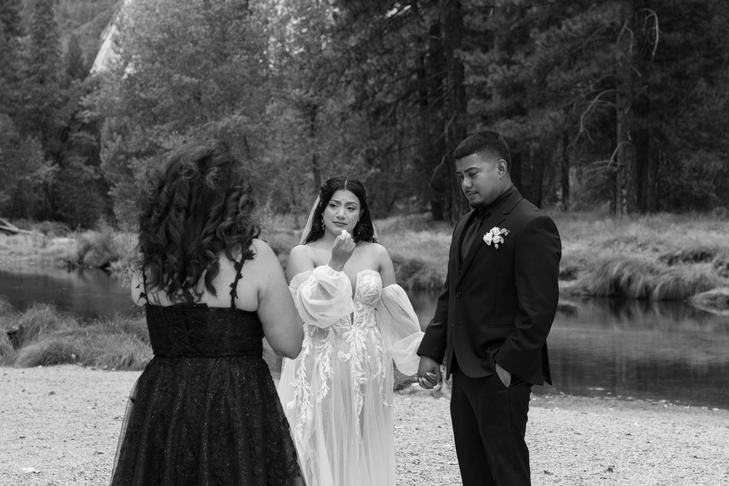 Wedding celebration by a serene lake with pine trees and mountains in background.