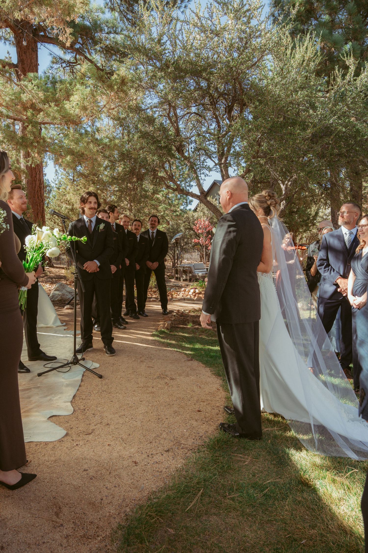 Wedding ceremony candid shot showing guests and wedding party gathered on a forest path.