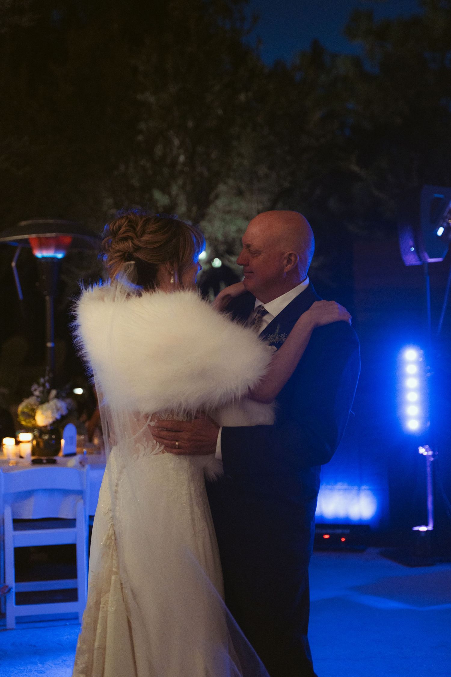 Couple dances under blue lighting at outdoor evening wedding reception.