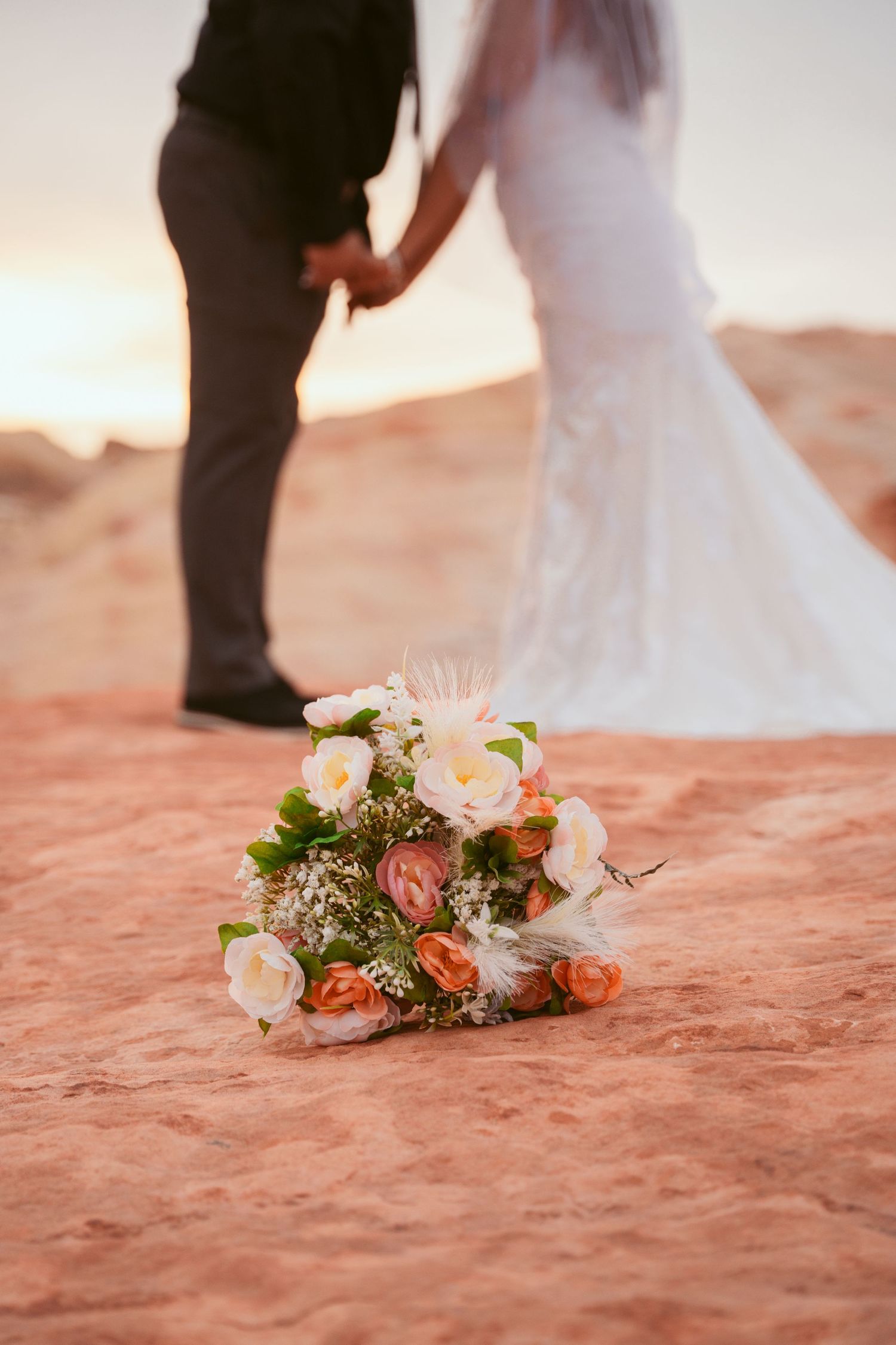 A bridal bouquet with pink and white flowers rests on red desert sand.