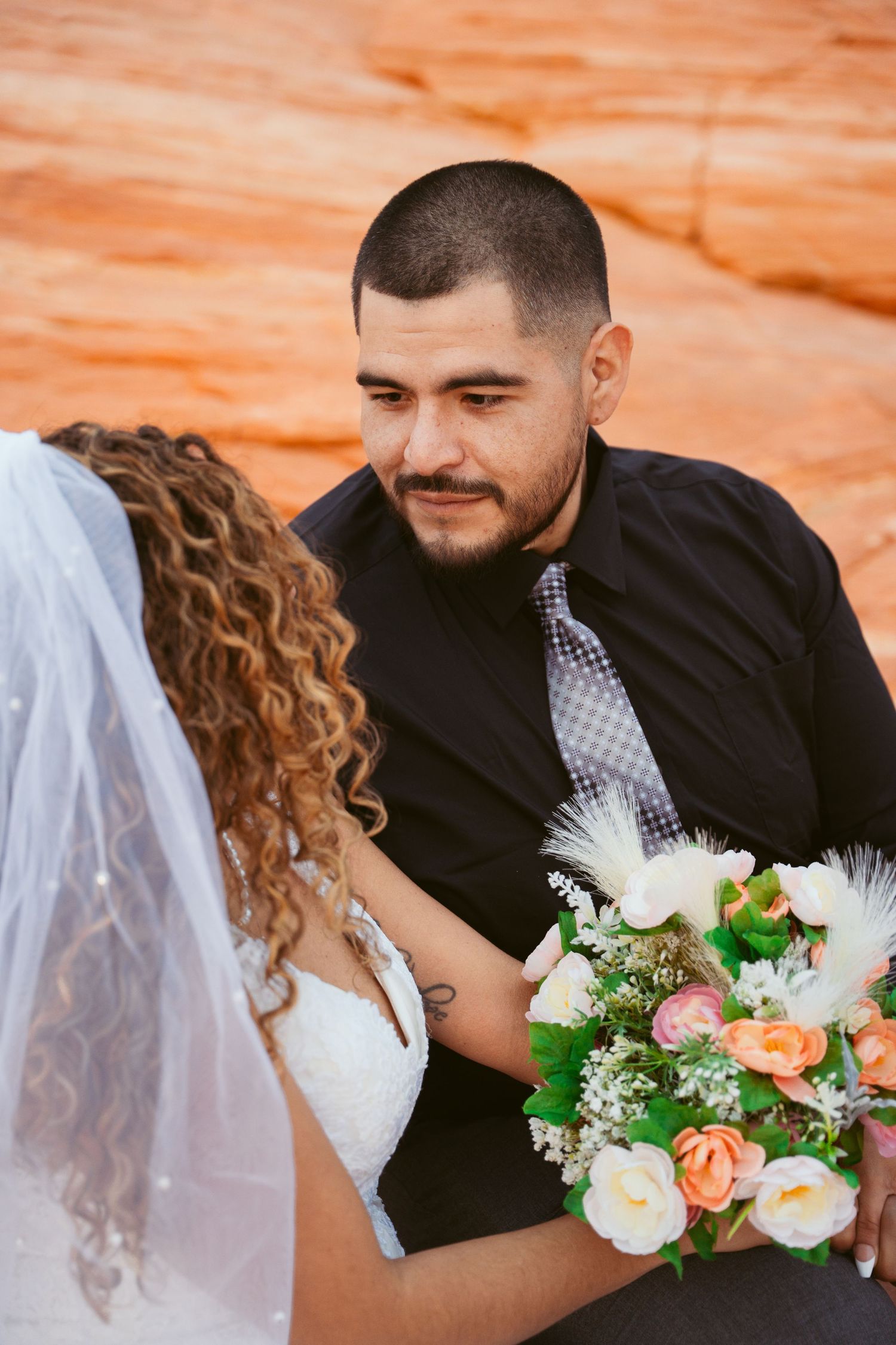 A newlywed couple embraces during their wedding photoshoot against red rock formations.