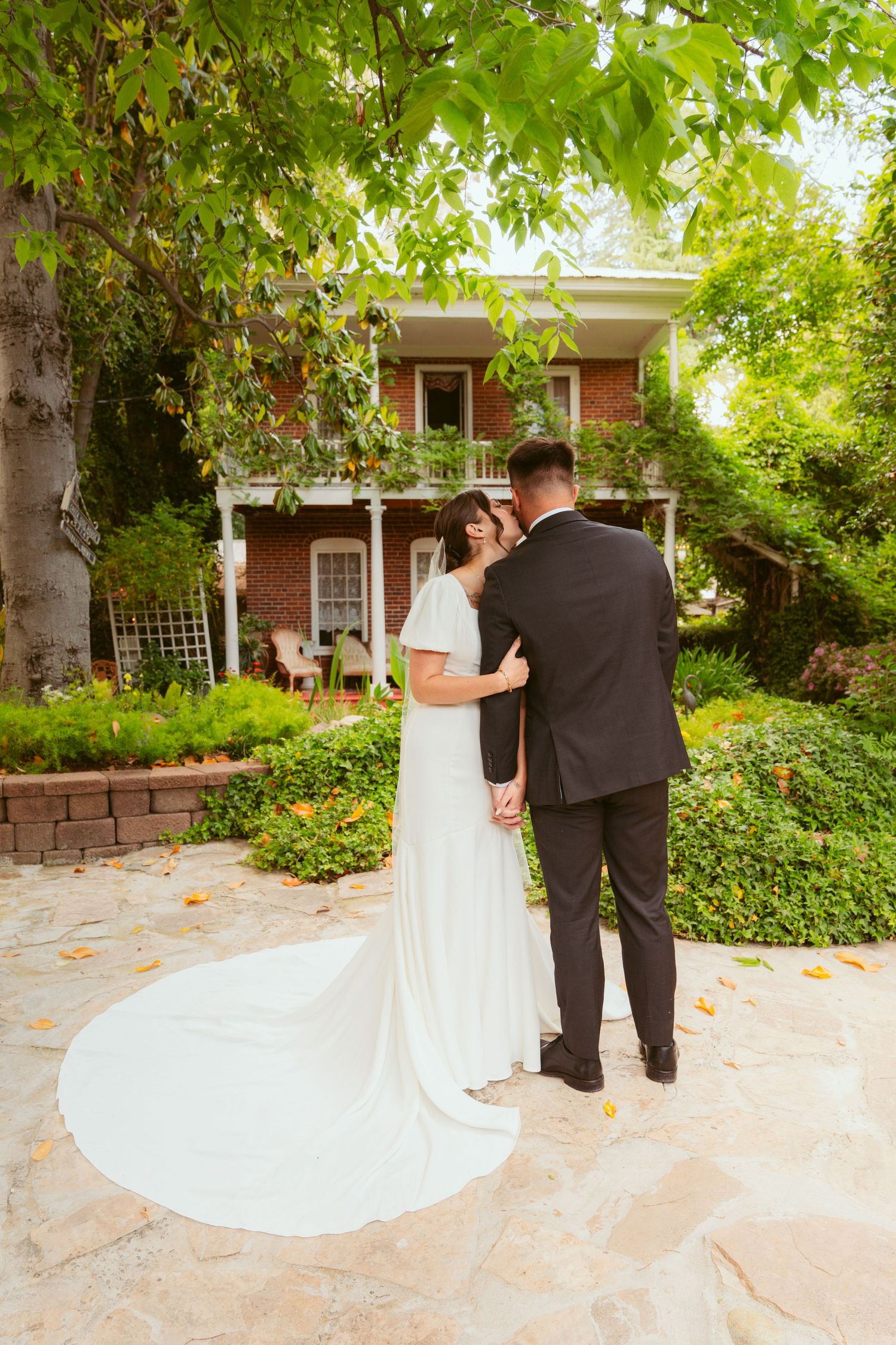 A wedding couple stands together on a stone patio surrounded by garden greenery.