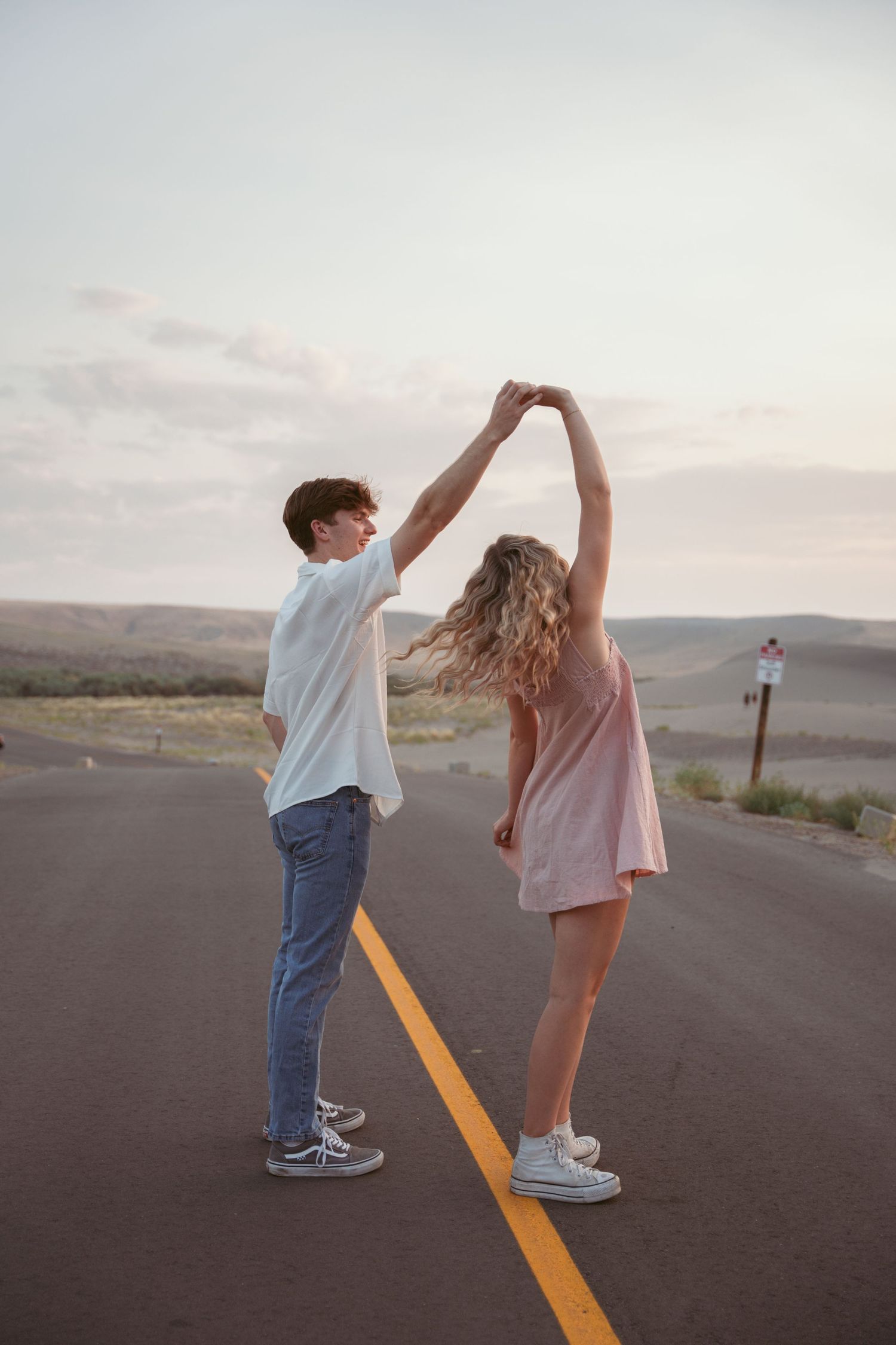 Two people dance together on a desert highway during golden hour.